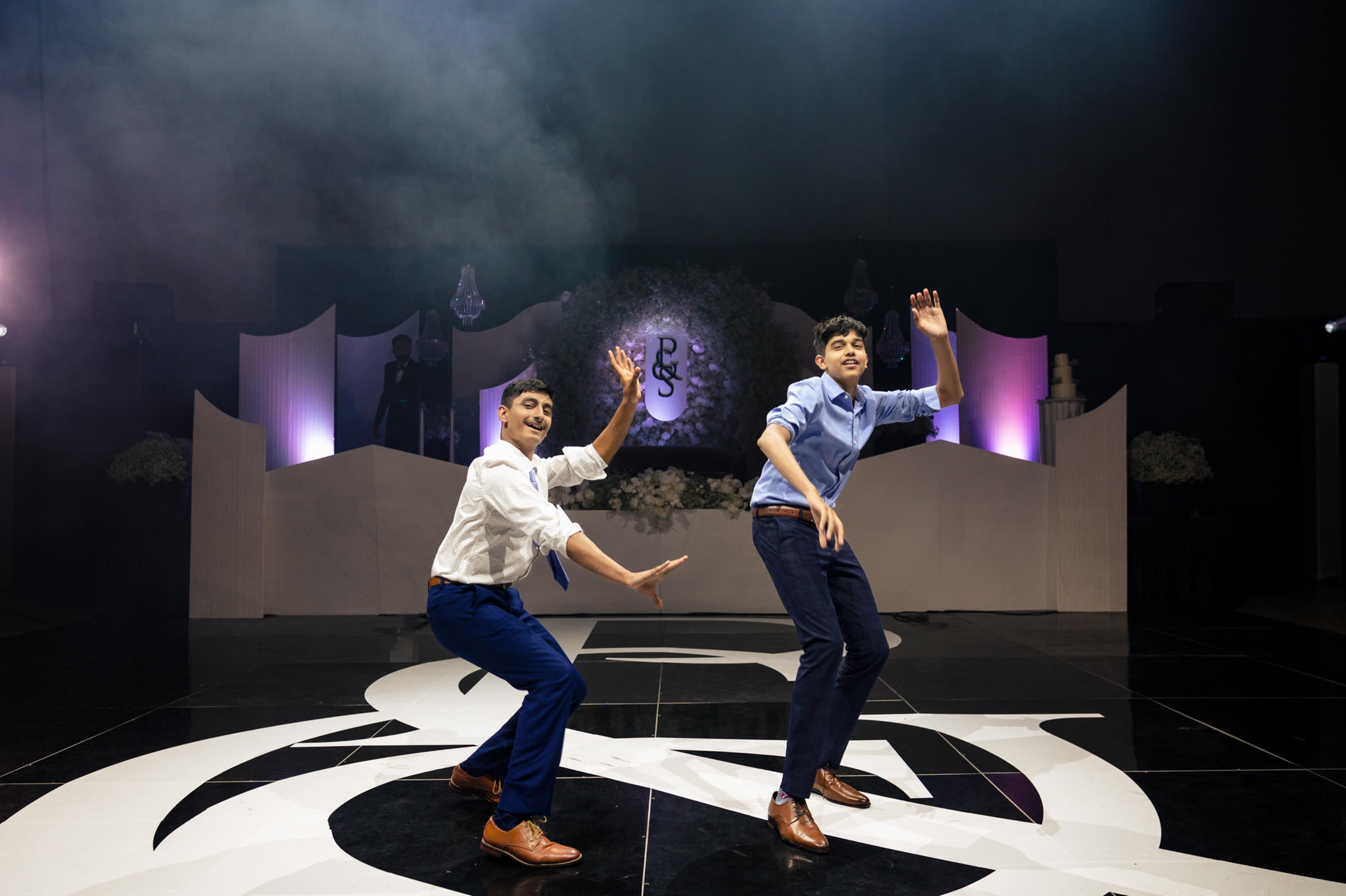 Two men energetically dance on a stage, as Winnipeg wedding lights dazzle in the background.