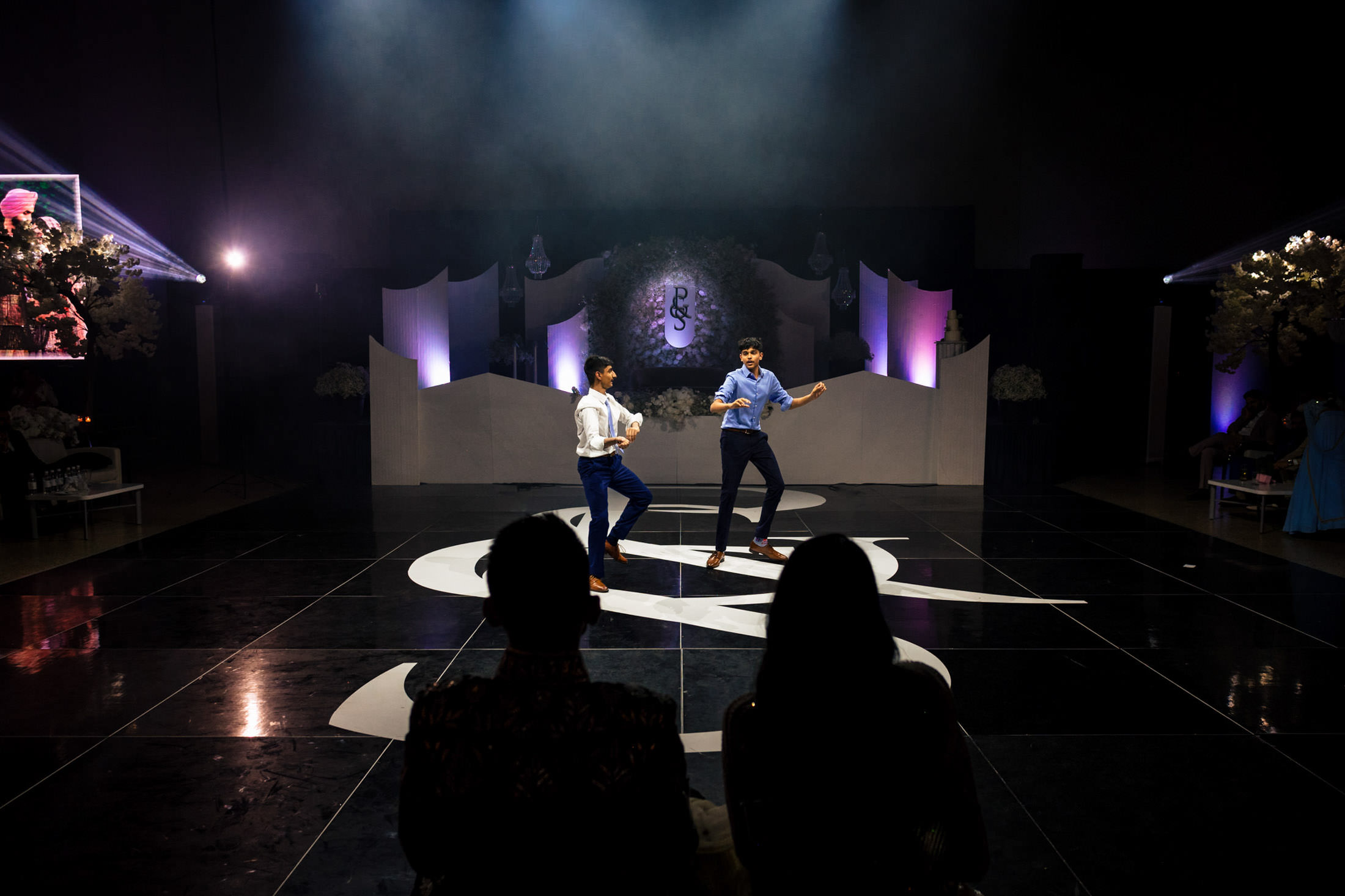 Two people dance on a dark stage, spotlighted at a Winnipeg wedding, with an audience watching.
