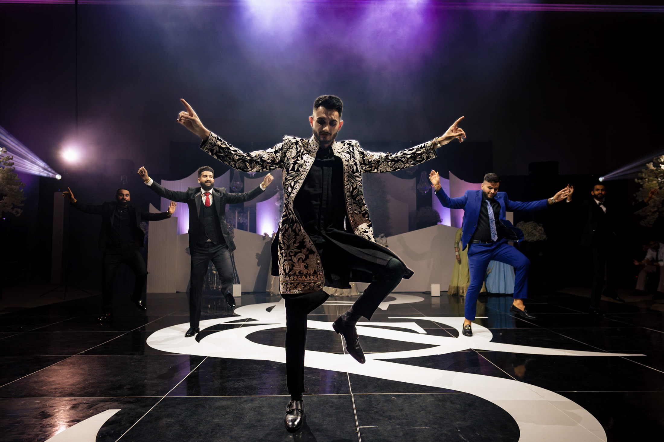 Men dancing energetically on a stage with colorful lighting at a Winnipeg wedding.
