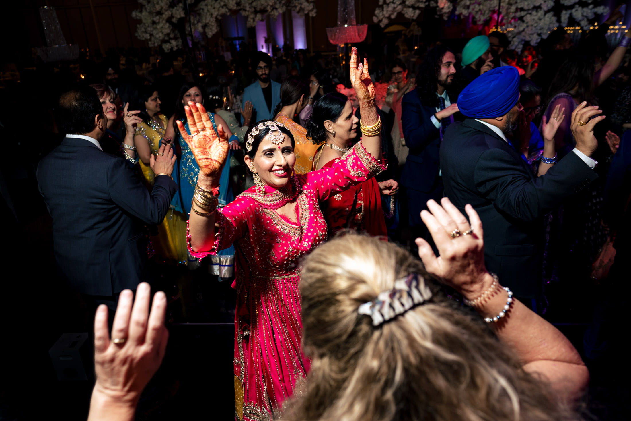 People dancing energetically at a Winnipeg wedding, woman in pink showing hennaed hands.
