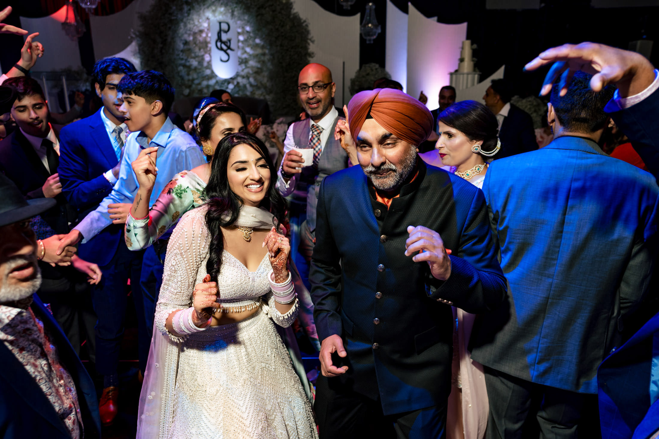 People dancing joyfully at a Winnipeg wedding, with festive attire and colorful lights.