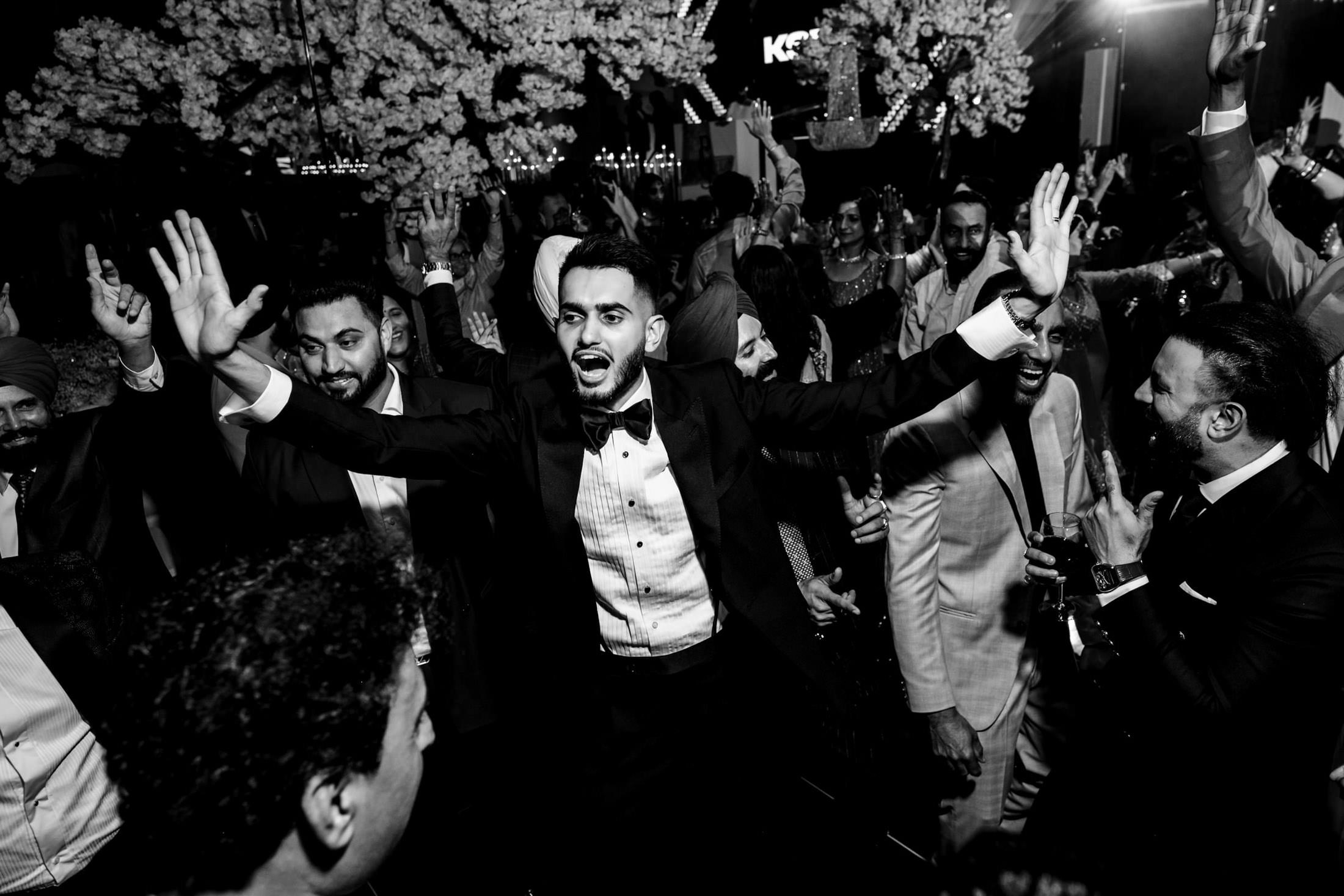 Man in suit joyfully dancing at a lively Winnipeg wedding with people around him.