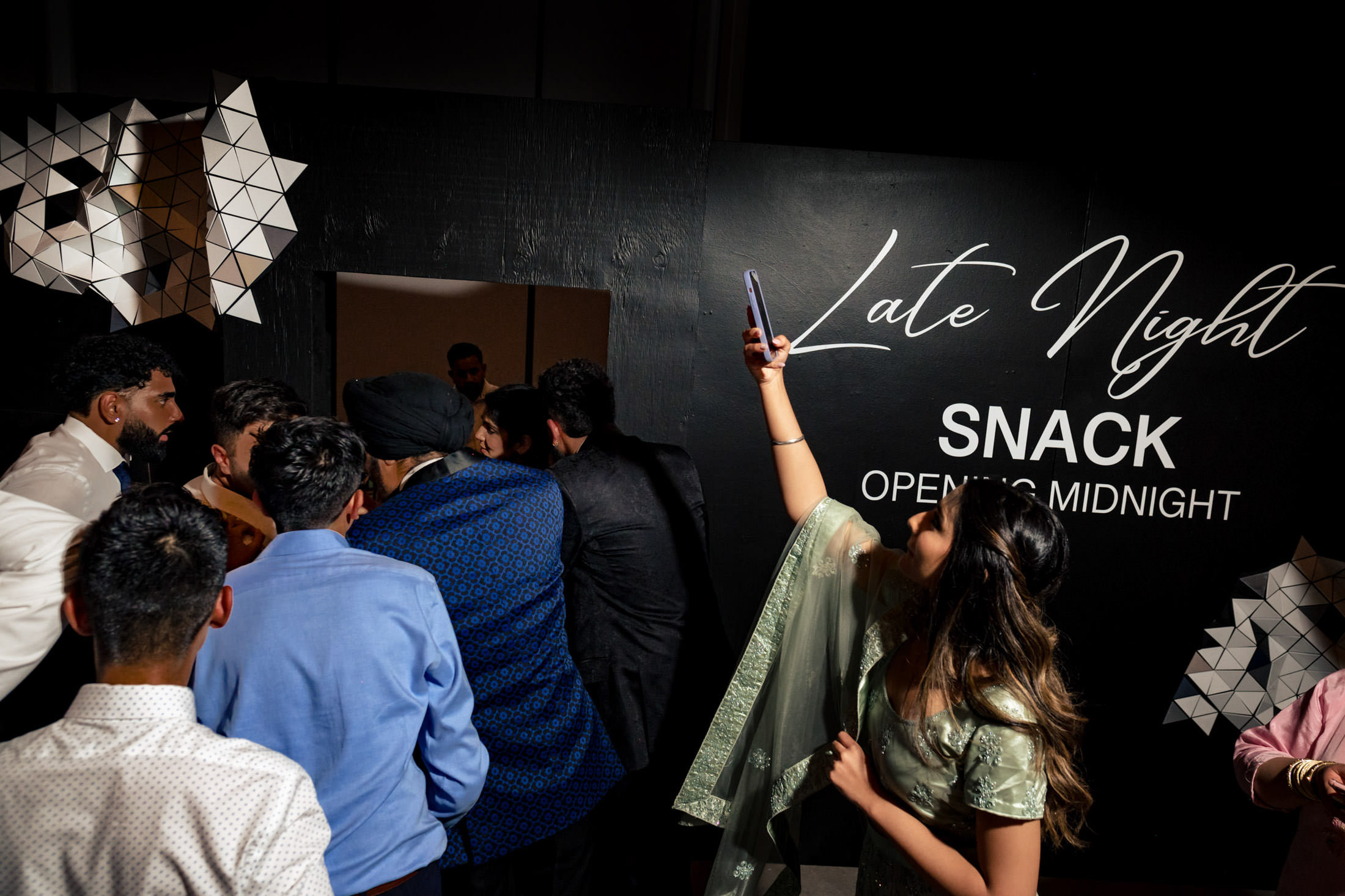 People waiting; a woman in a green dress takes a selfie. Sign says "Late Night Snack.