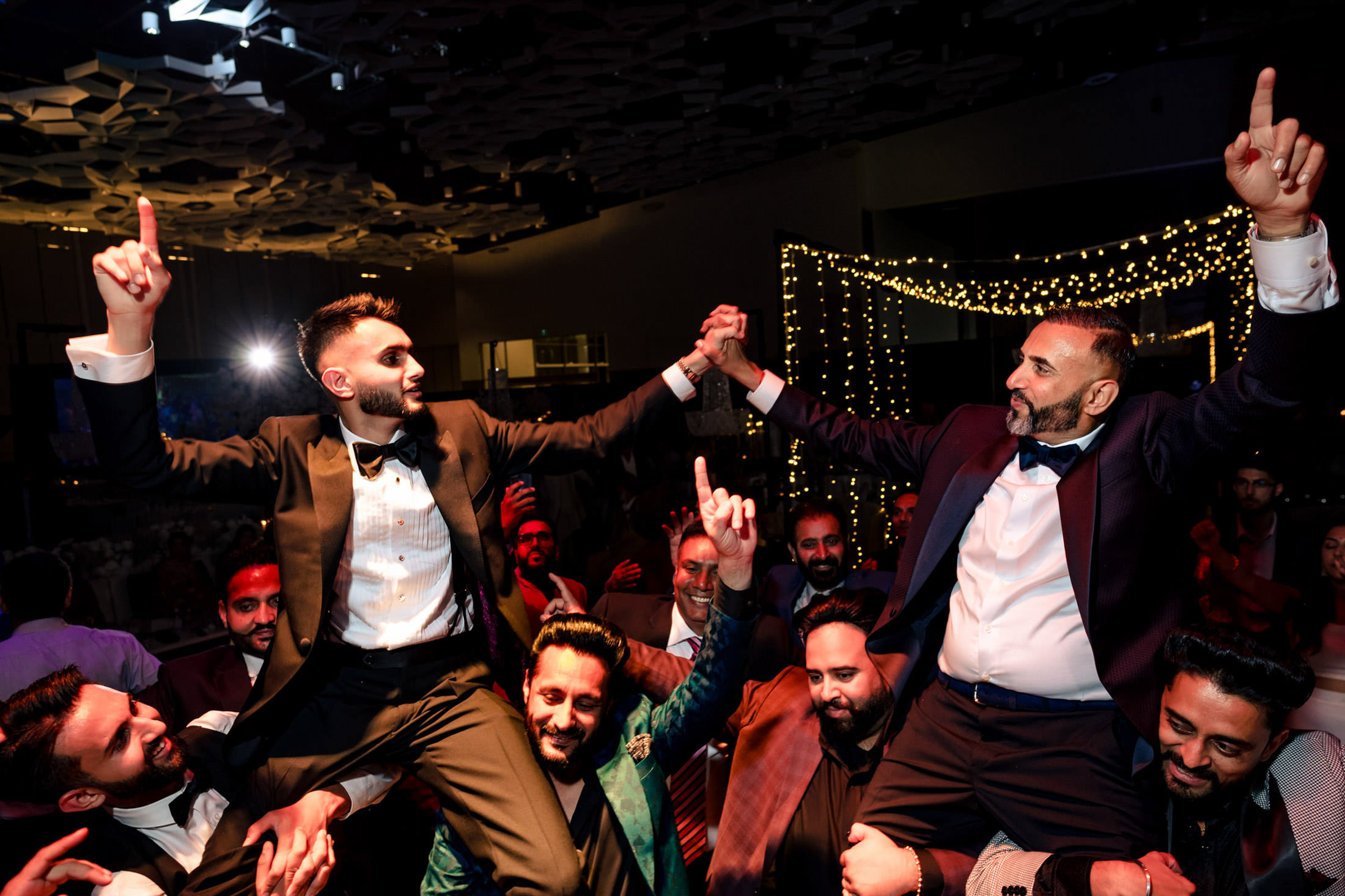 Two men in suits are lifted up and cheering at a lively Winnipeg wedding celebration.
