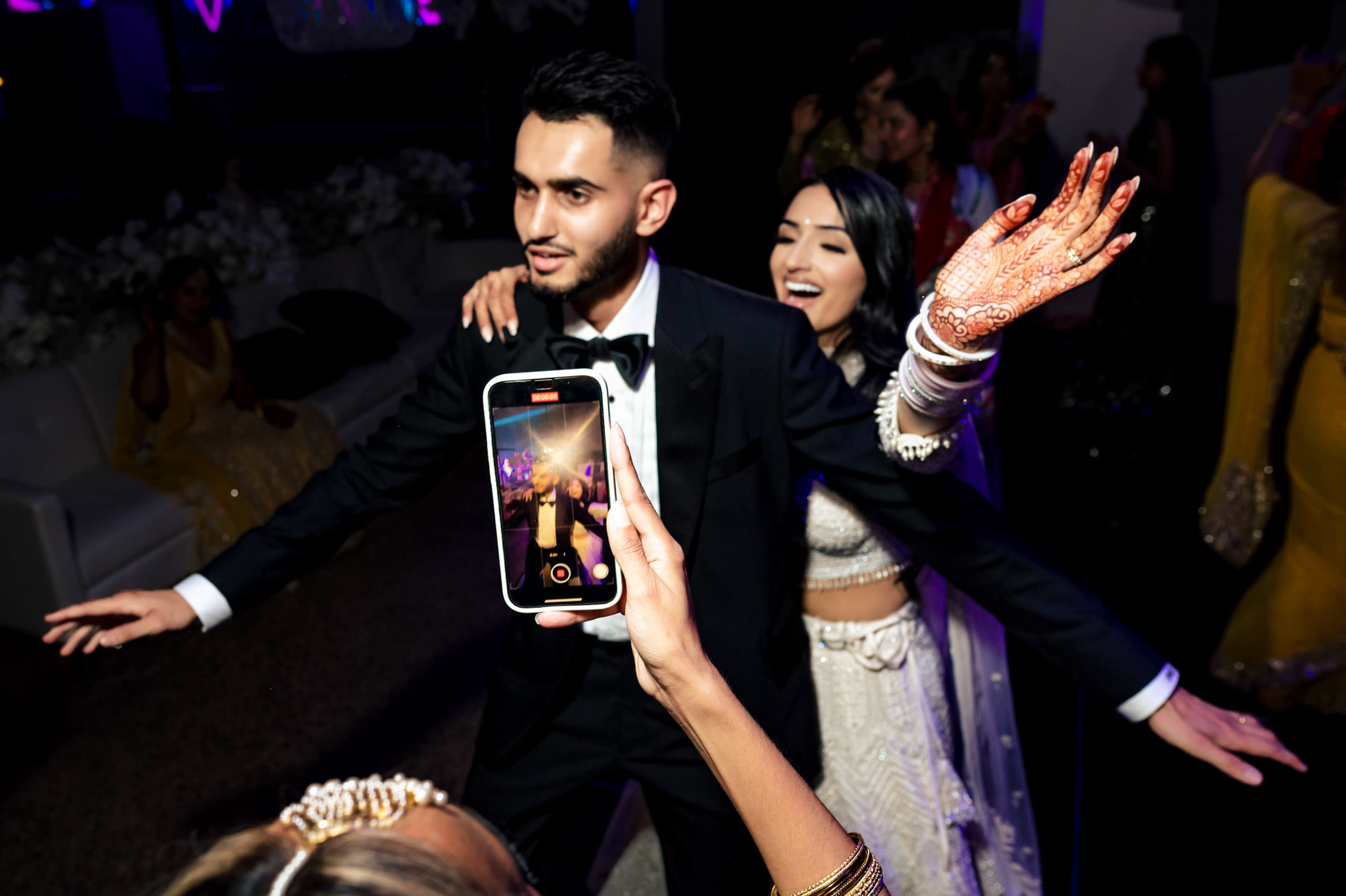 A couple dances joyfully at a Winnipeg wedding, captured on a phone camera in the foreground.