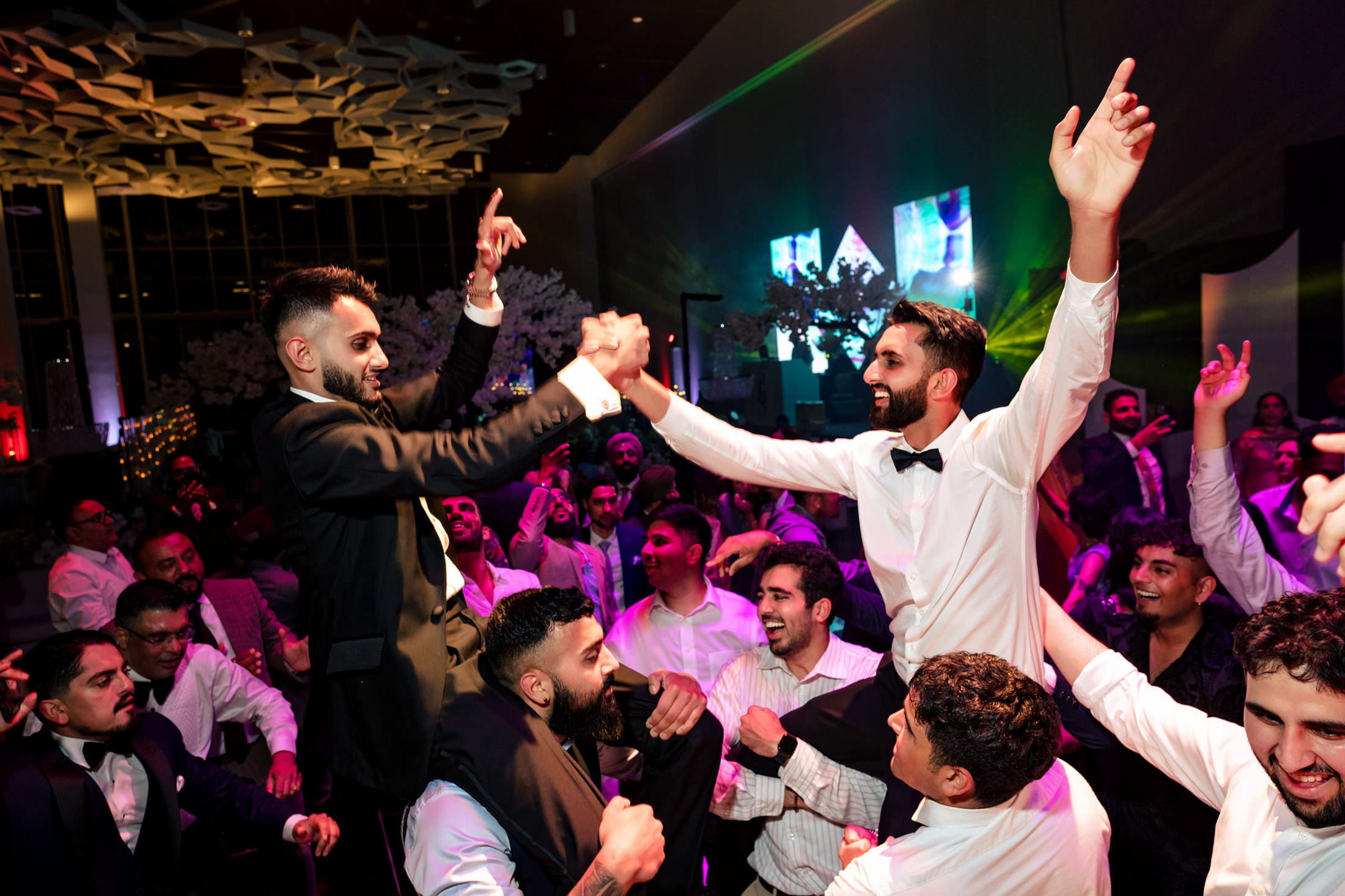Group of people dancing and celebrating at a lively Winnipeg wedding with colorful lighting.