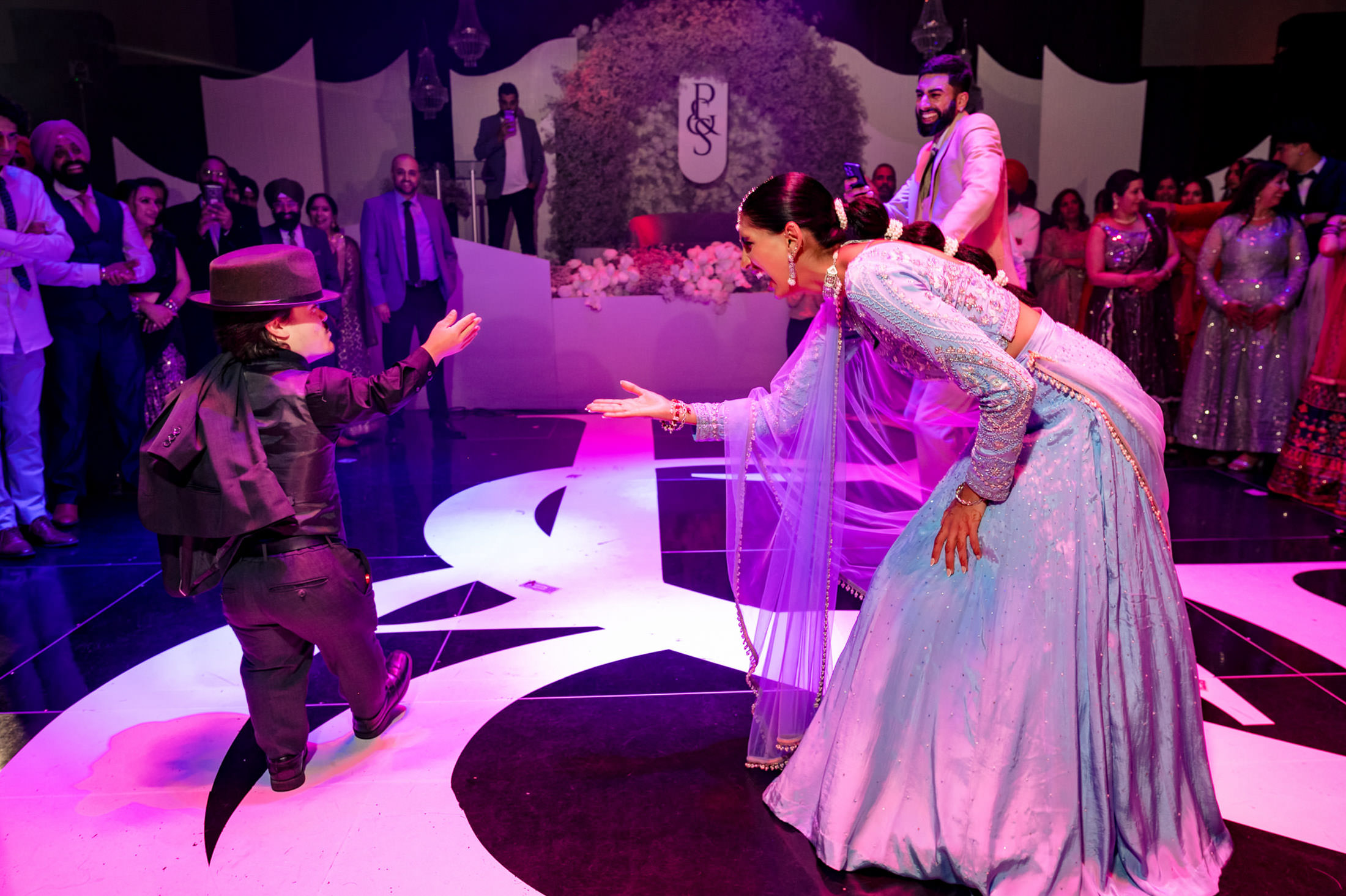 A woman dances with a child in a hat on a vibrant Winnipeg wedding stage, surrounded by guests.