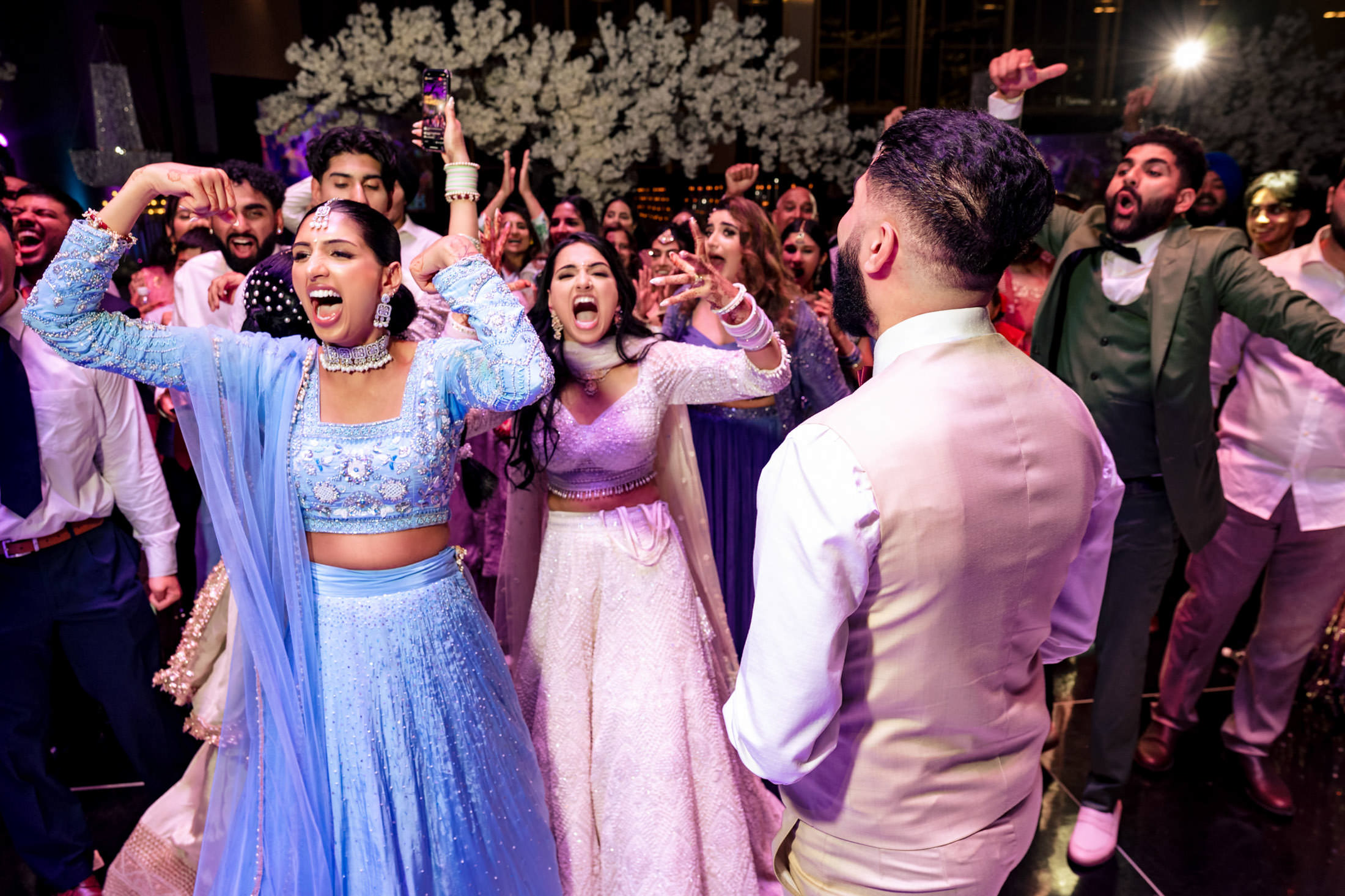 A joyful group dances energetically at a lively Winnipeg wedding with floral decor.
