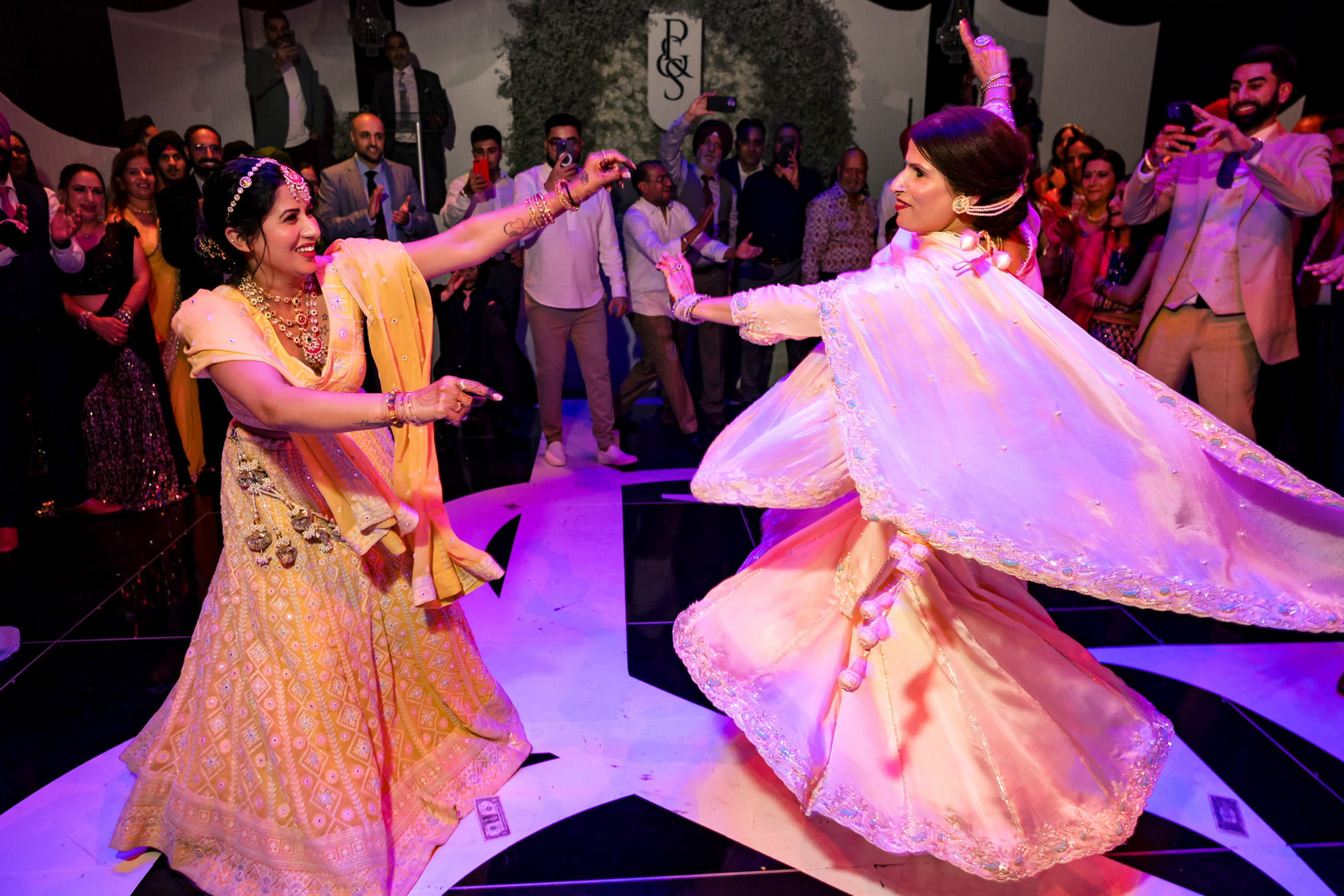 Two women in ornate dresses dancing joyfully at a lively Winnipeg wedding celebration.