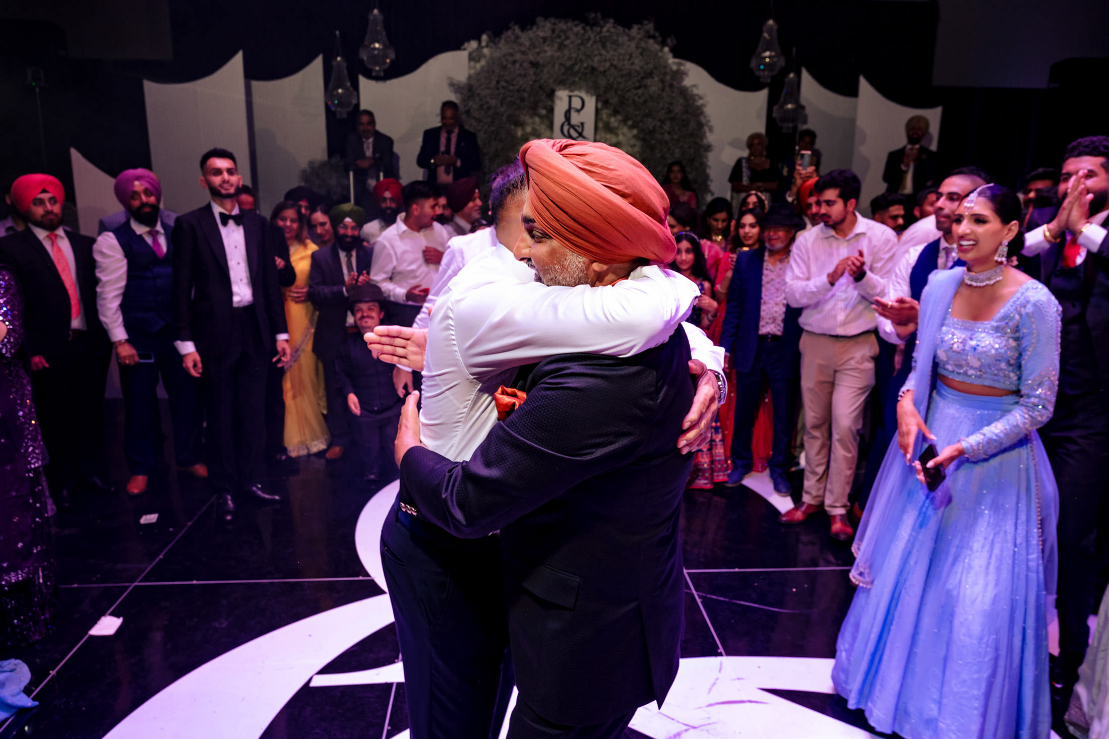 Two men hugging at a lively Winnipeg wedding, surrounded by clapping guests.