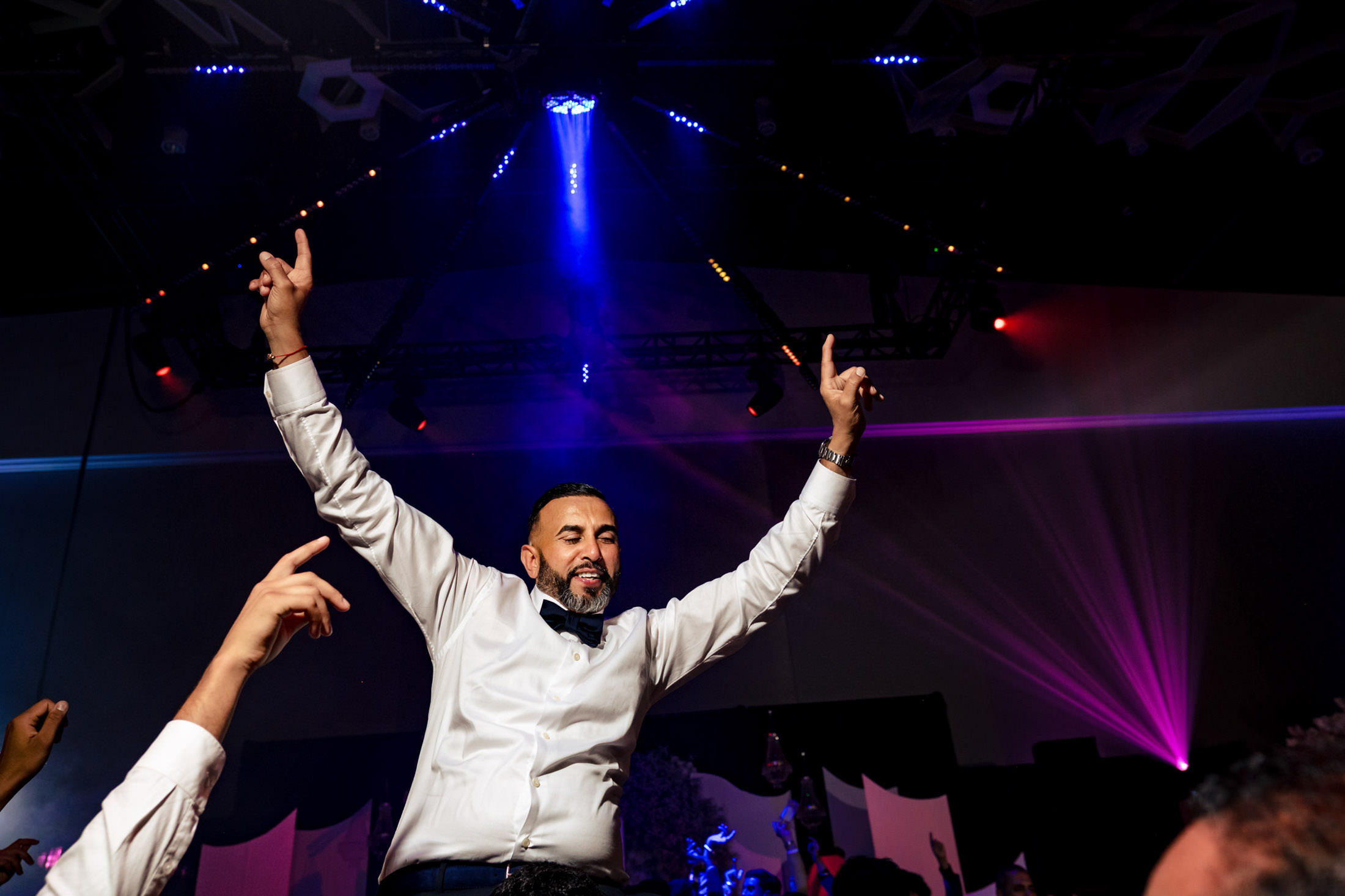 Man in white shirt celebrates at Winnipeg wedding under colorful stage lights.