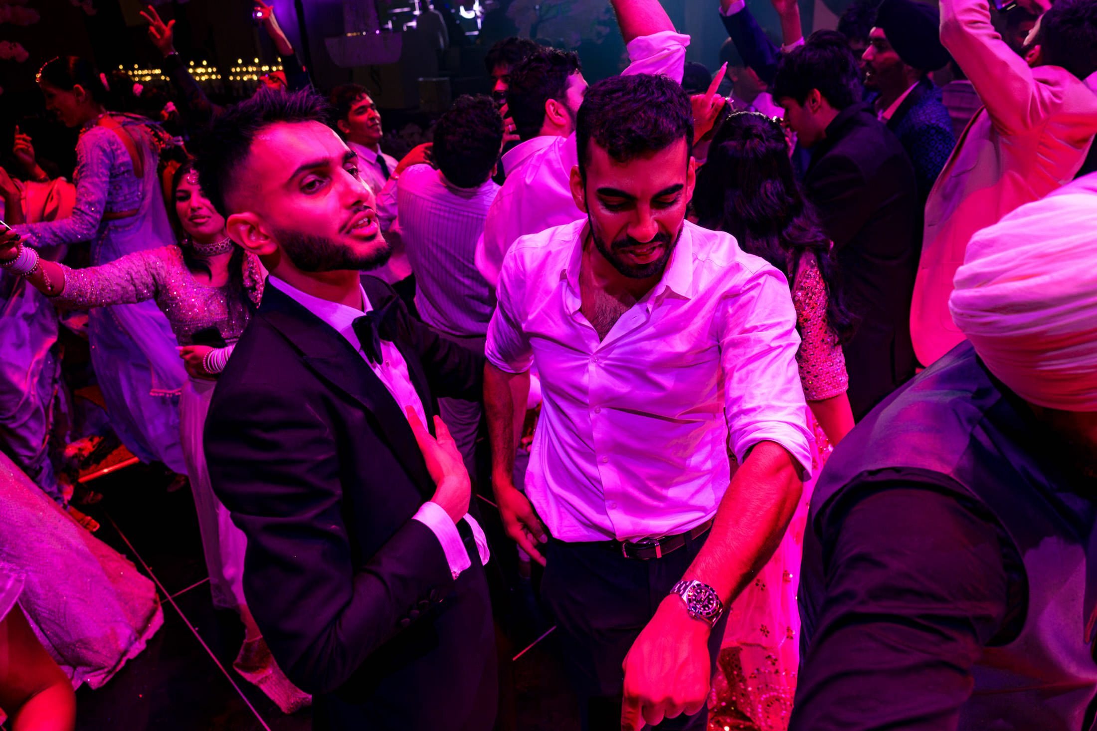 People dancing energetically at a Winnipeg wedding in vibrant, colorful lighting.