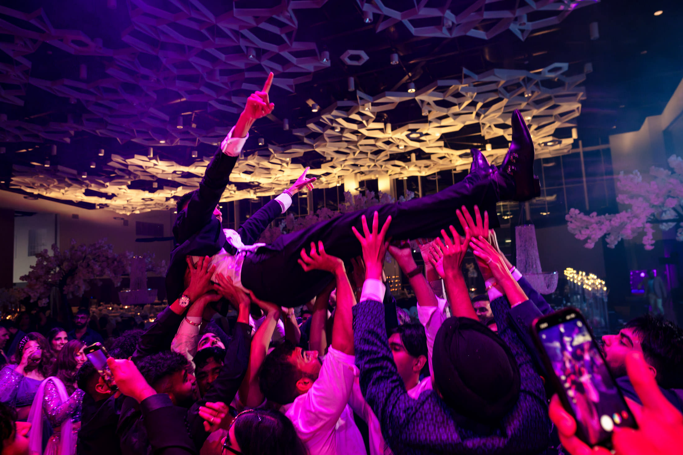 A man in a suit is crowd-surfed at a lively Winnipeg wedding with colorful lighting.