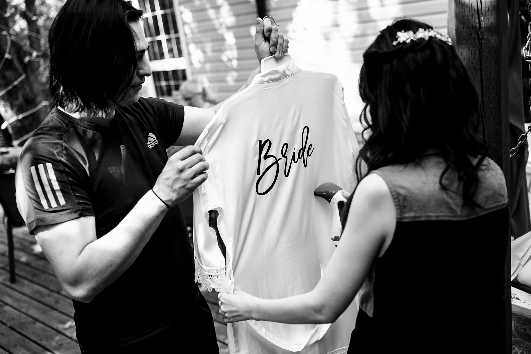 Two people holding a "Bride" robe at Ashgrove Acres Wedding, in black and white.
