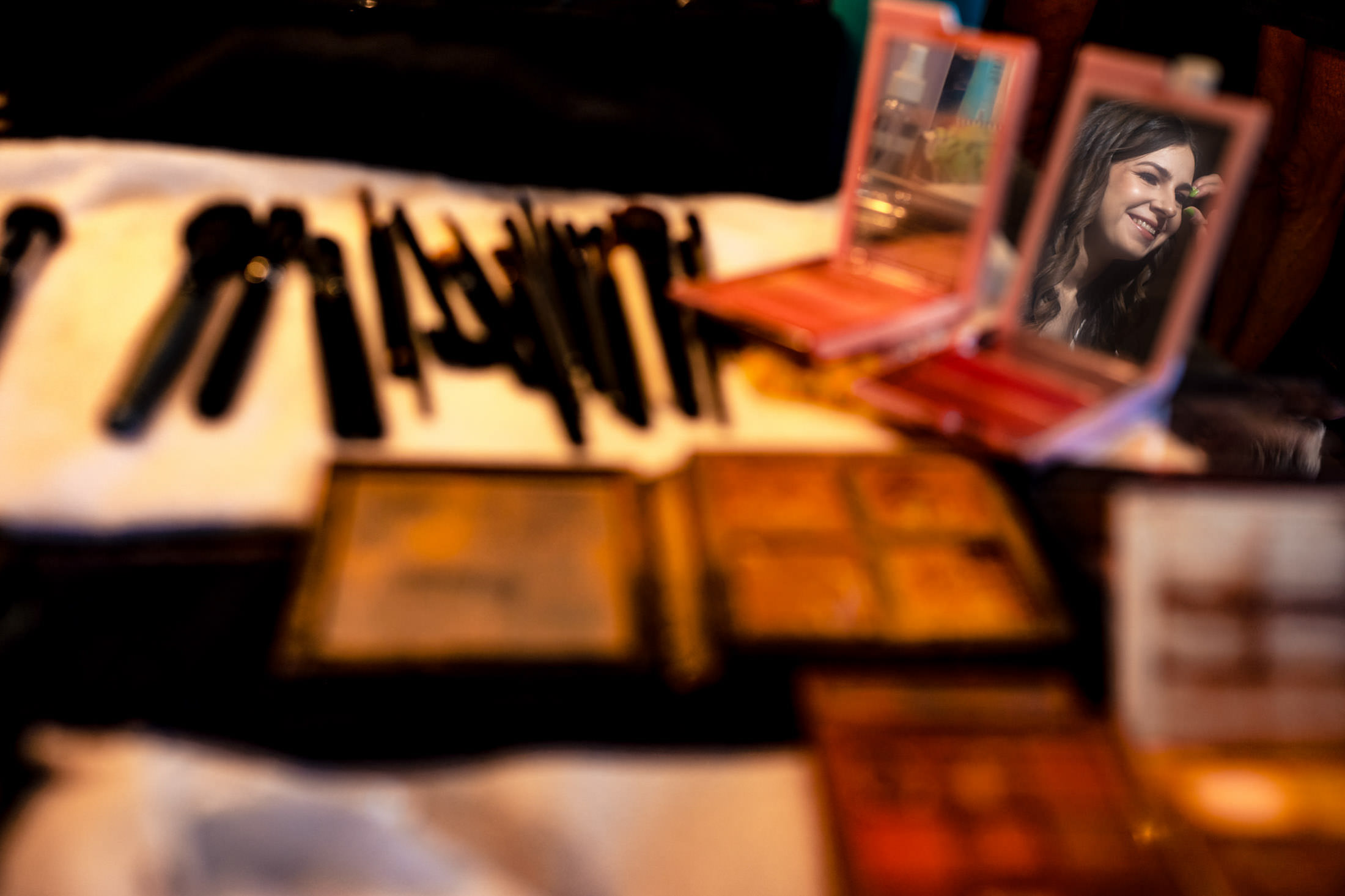 Reflection of a woman at Ashgrove Acres with makeup brushes and palettes on the table.