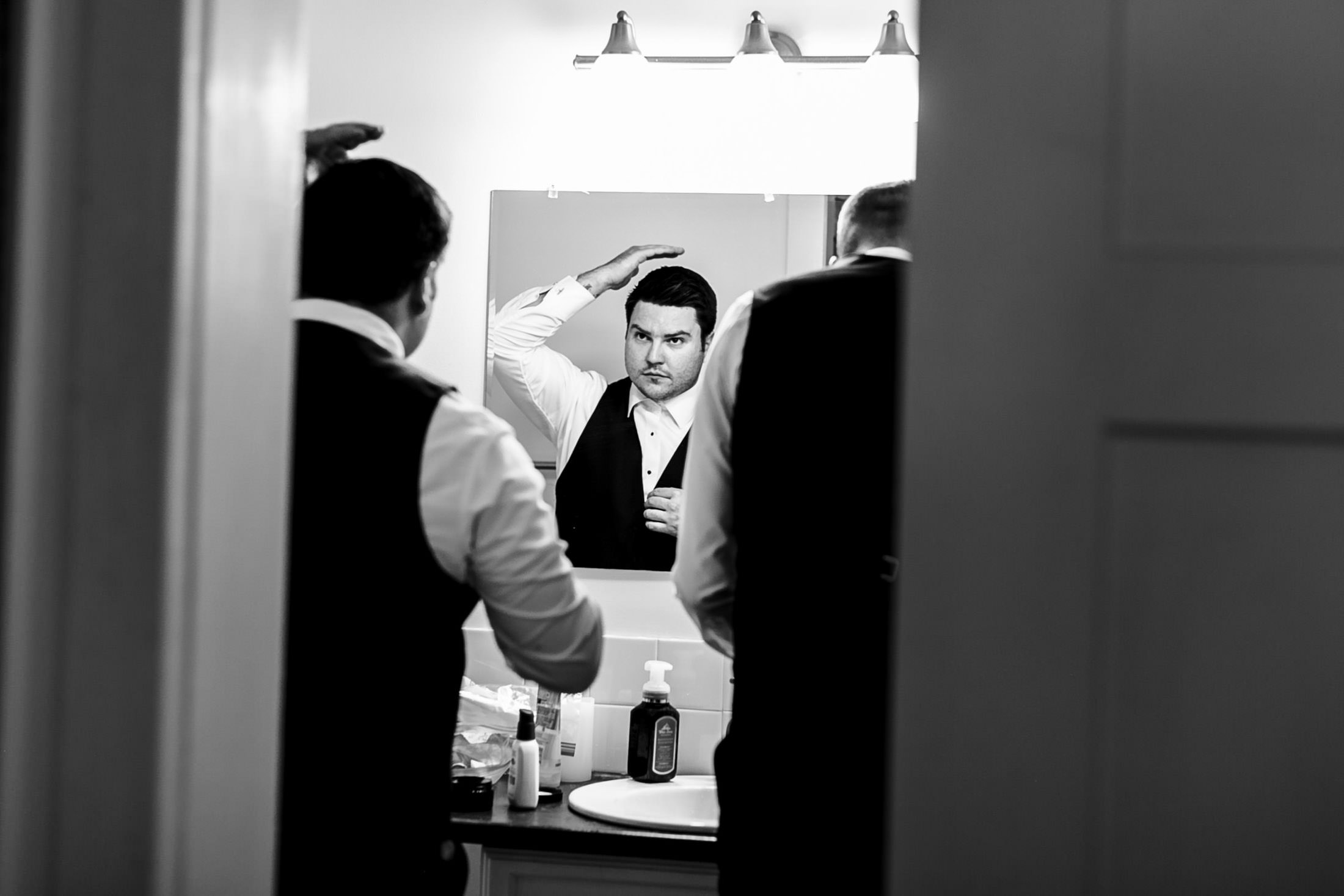 Man in suit fixing hair in bathroom mirror, a moment before the Ashgrove Acres wedding.