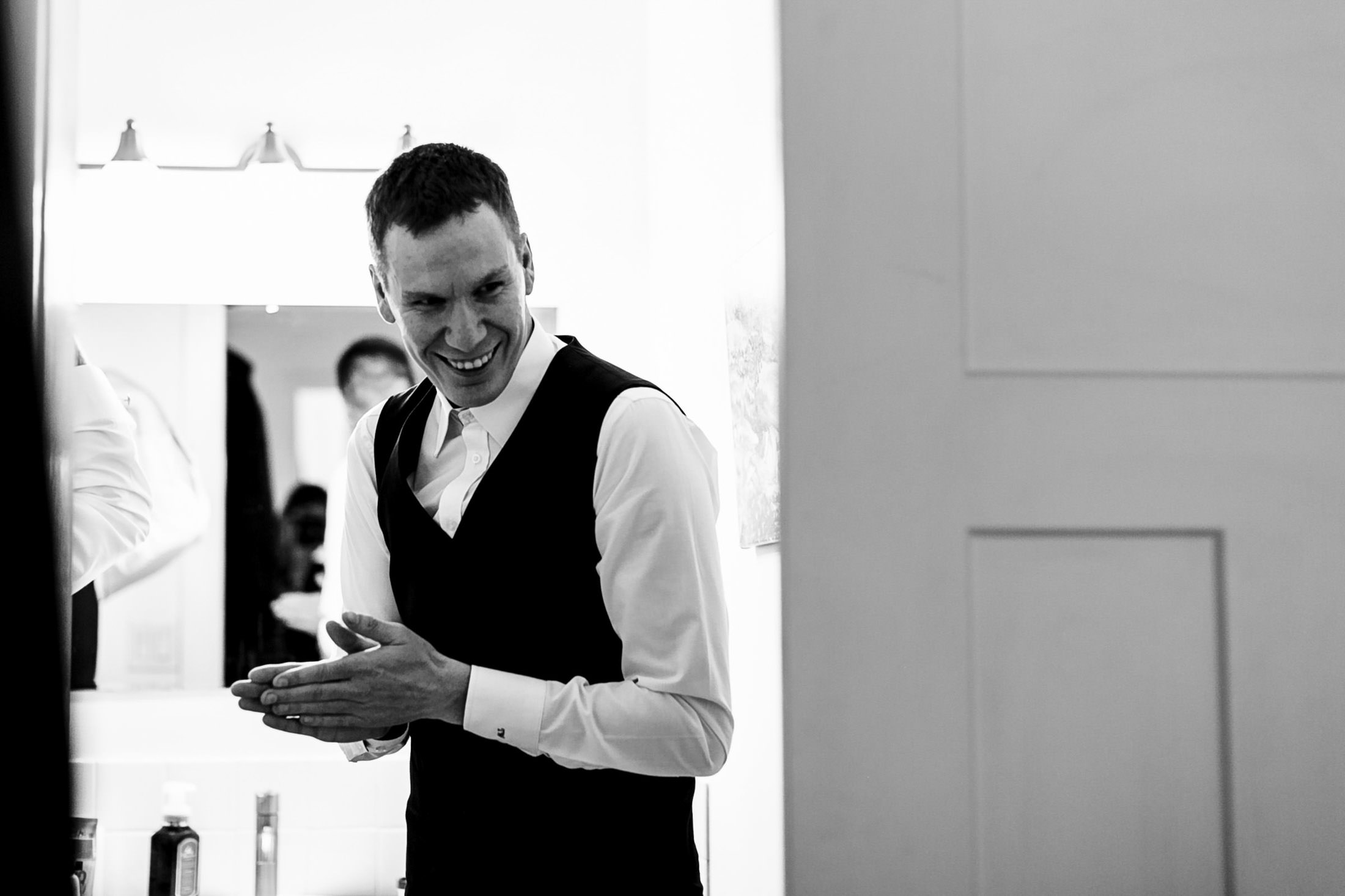 Man in vest claps hands, smiling by a mirror at Ashgrove Acres Wedding.