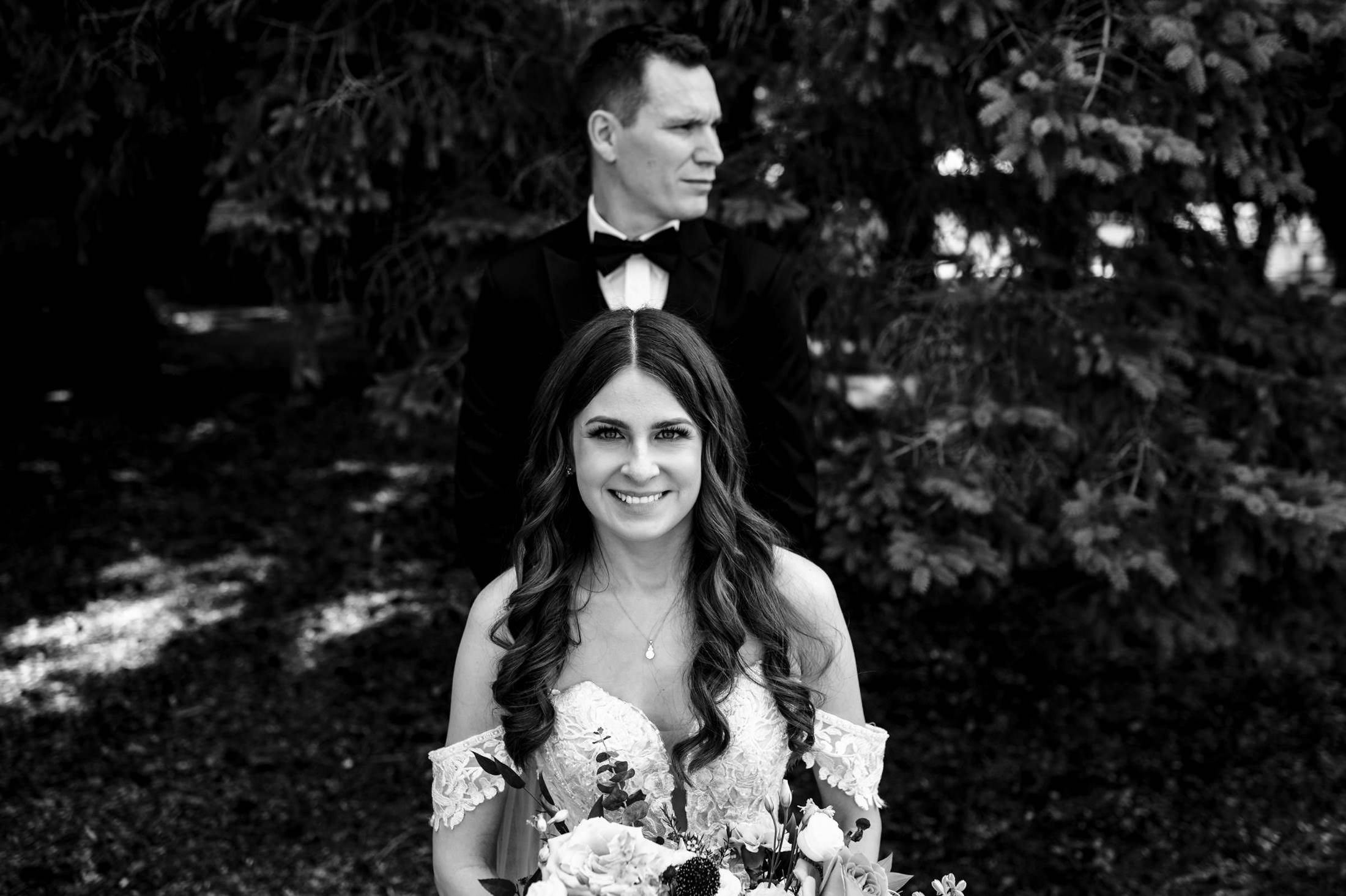 Bride smiling in front of groom at Ashgrove Acres, both in formal attire, outdoors.