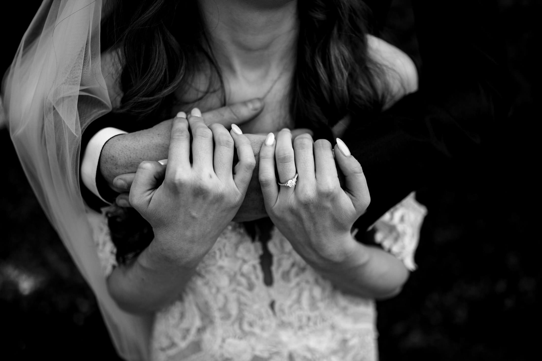 Bride and groom embrace at Ashgrove Acres, hands entwined in black and white elegance.