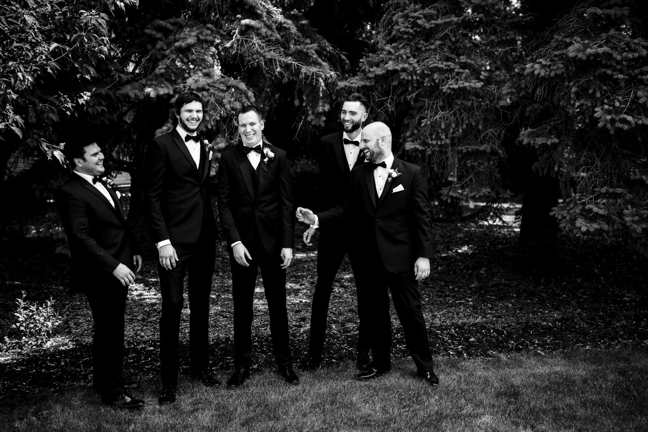 Five men in suits laughing together outdoors at an Ashgrove Acres wedding.
