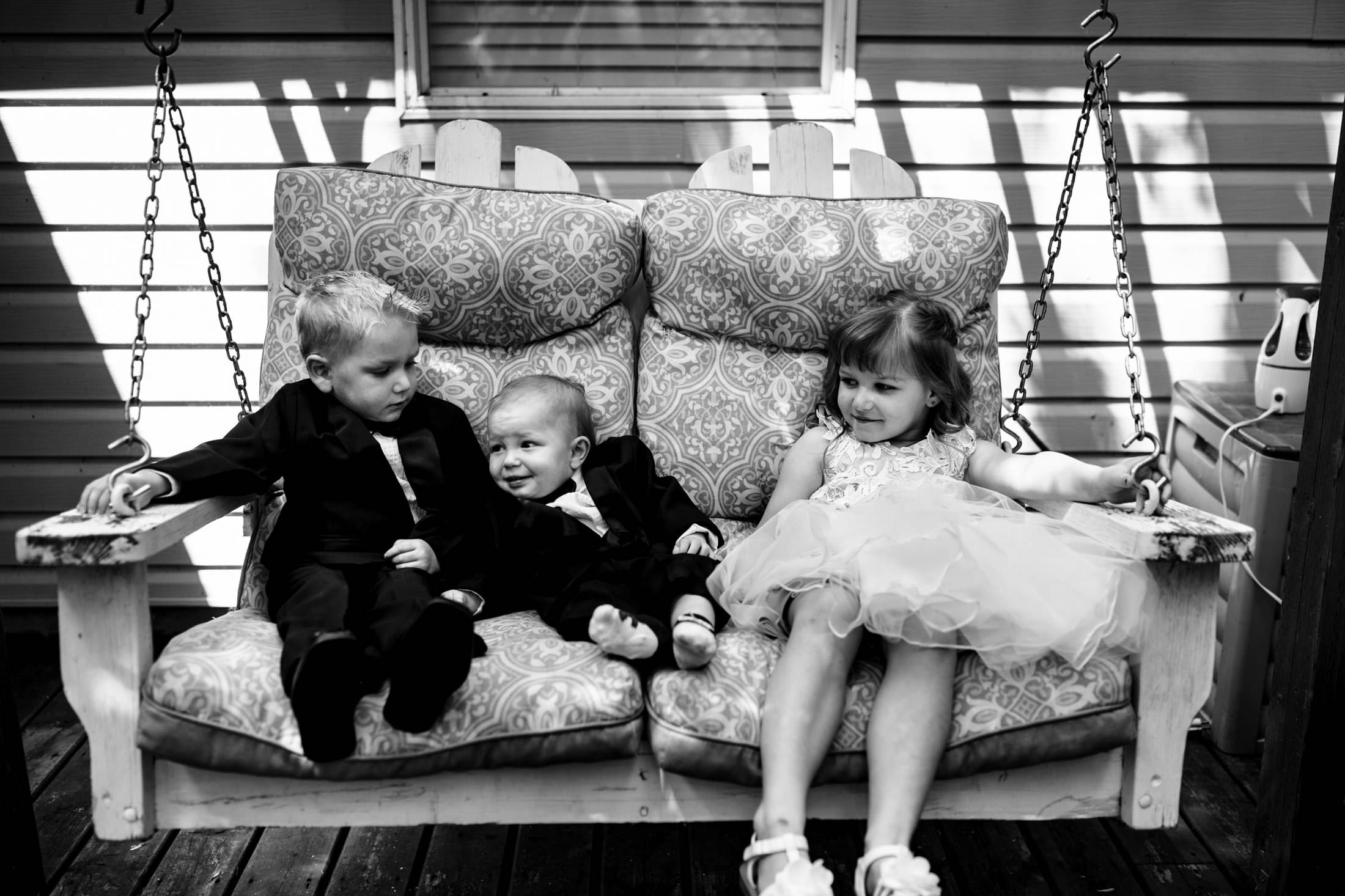 Three children in formal wear sit on a porch swing at Ashgrove Acres Wedding.