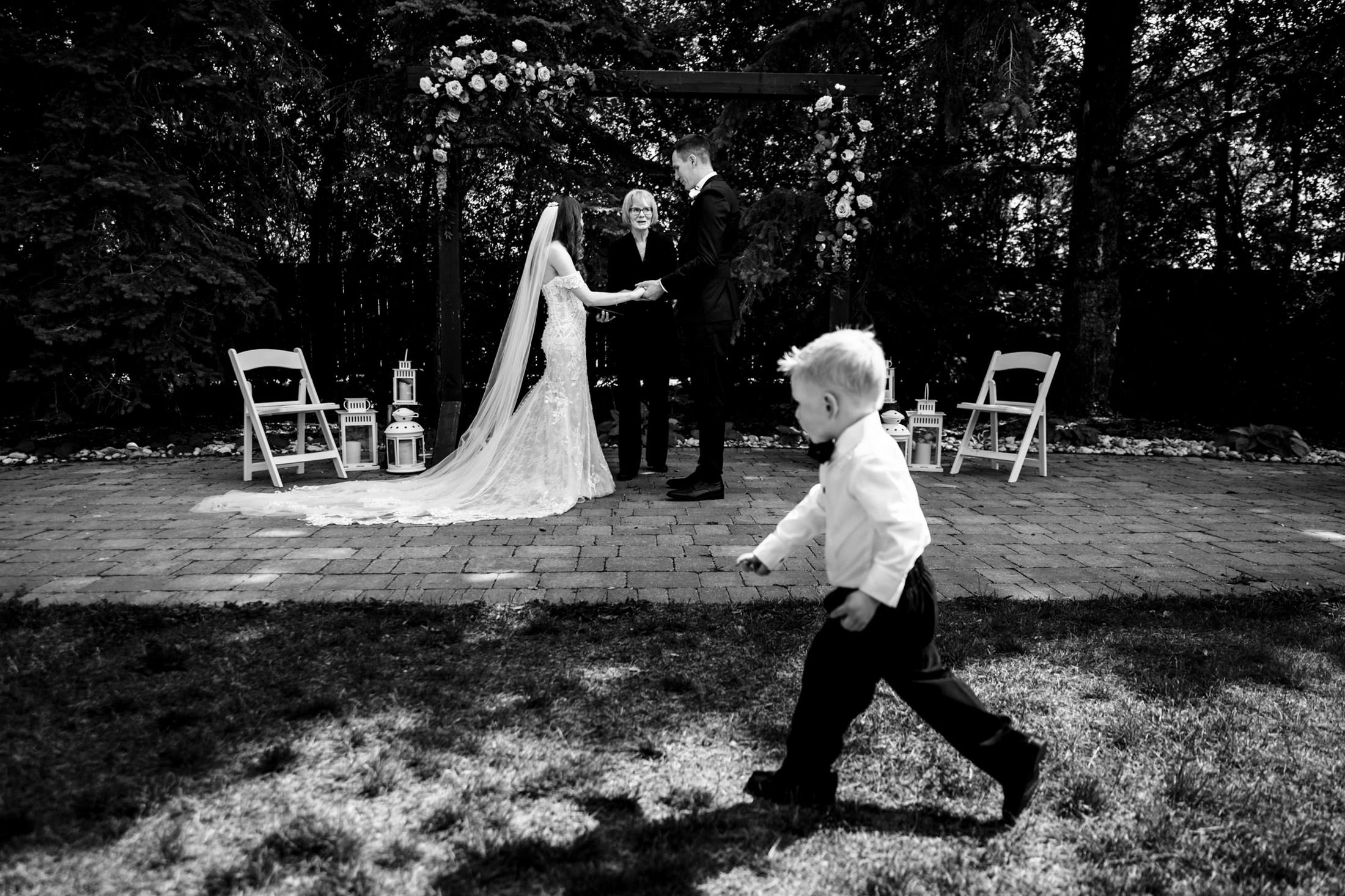A child in a suit dashes by as vows are exchanged at an Ashgrove Acres Wedding.