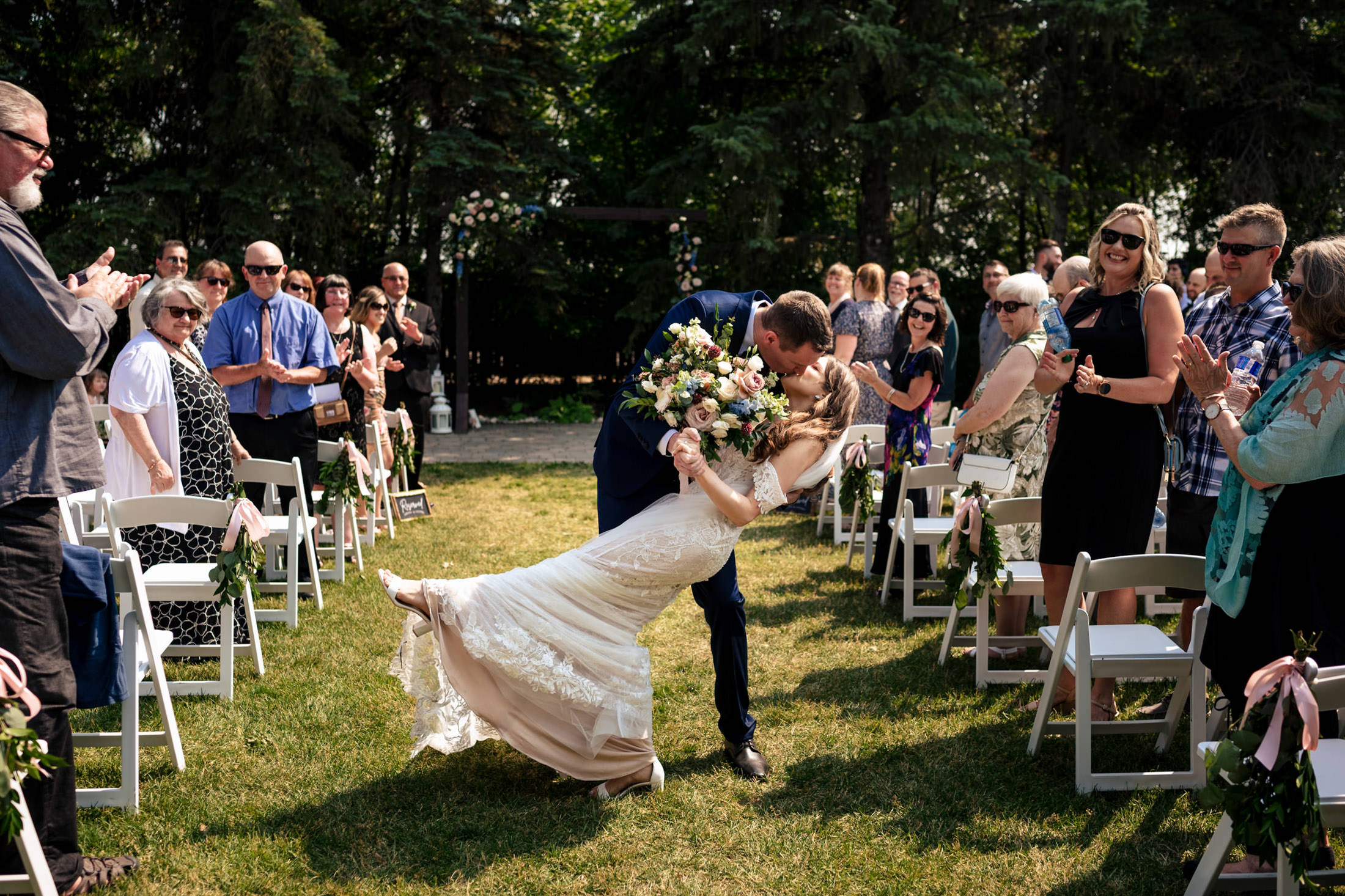 Bride and groom kiss at Ashgrove Acres, surrounded by clapping guests.