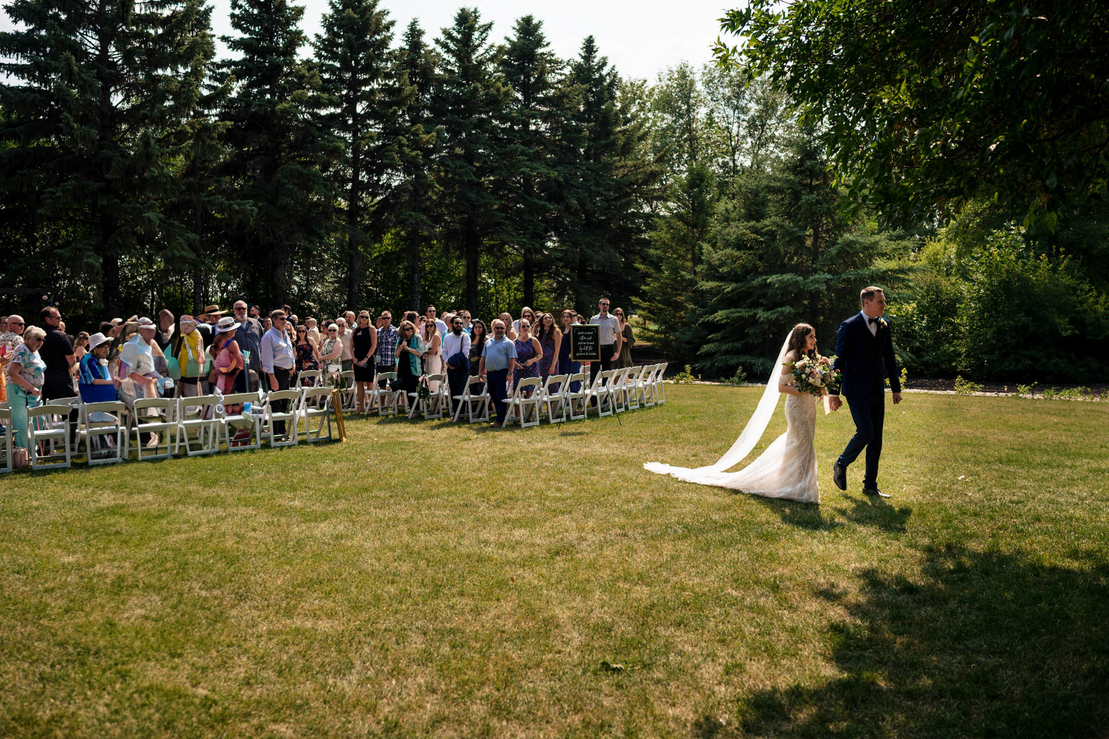 The bride and groom stroll down the aisle at Ashgrove Acres under a sunny sky.