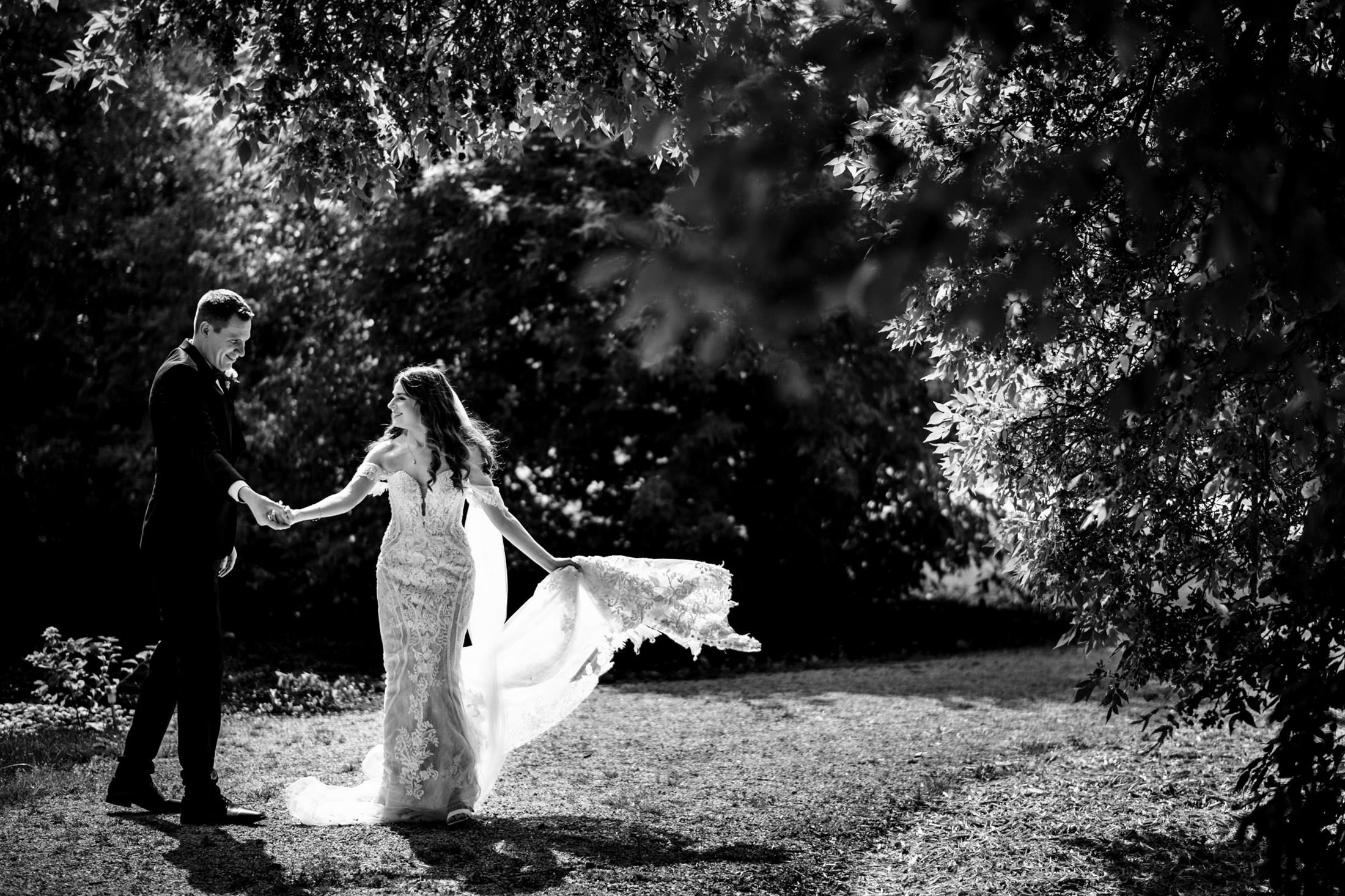 Bride and groom at Ashgrove Acres joyfully holding hands, her dress flowing in the sunlit garden.