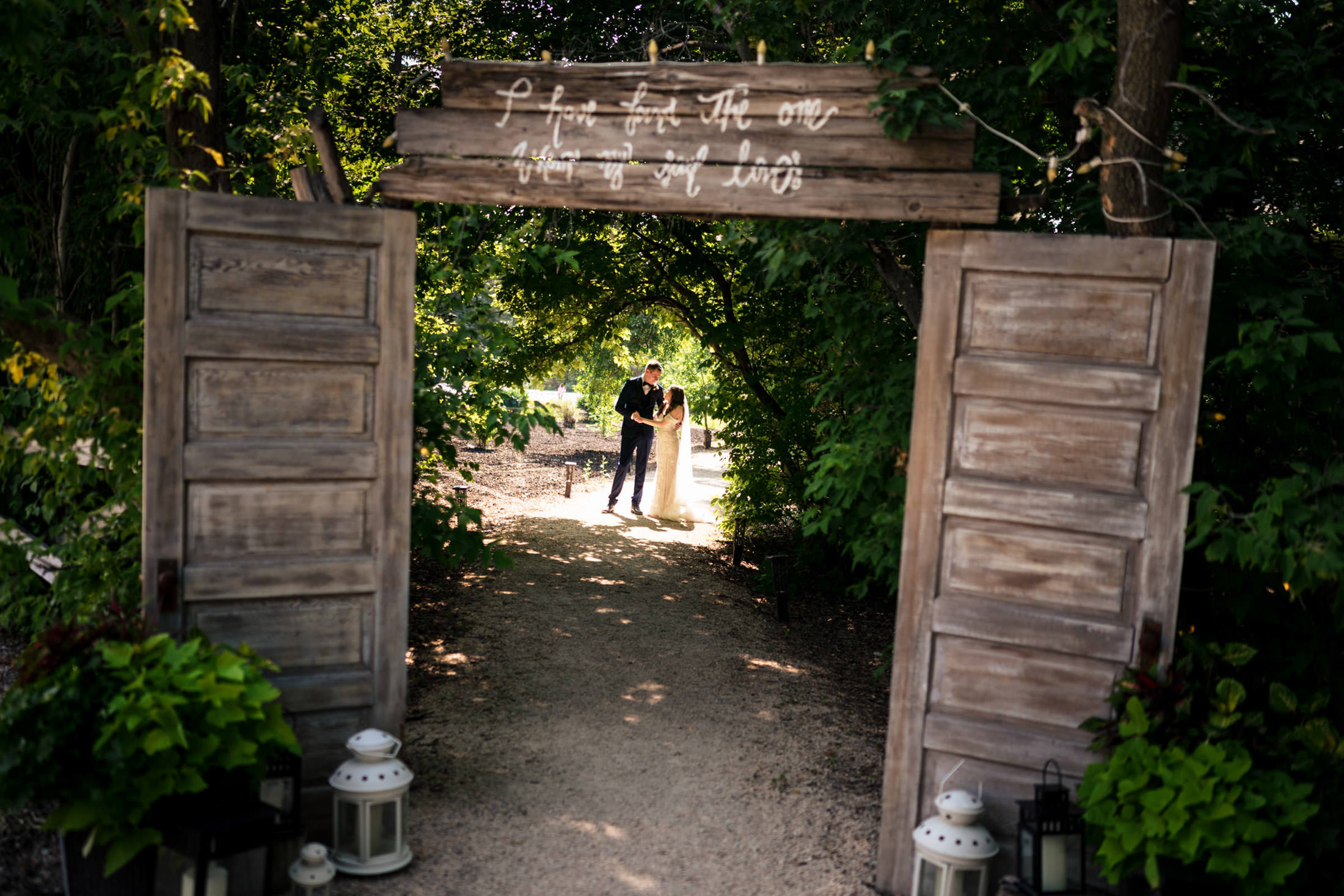 Rustic wooden doorway frames a couple at Ashgrove Acres on a sunlit garden path.
