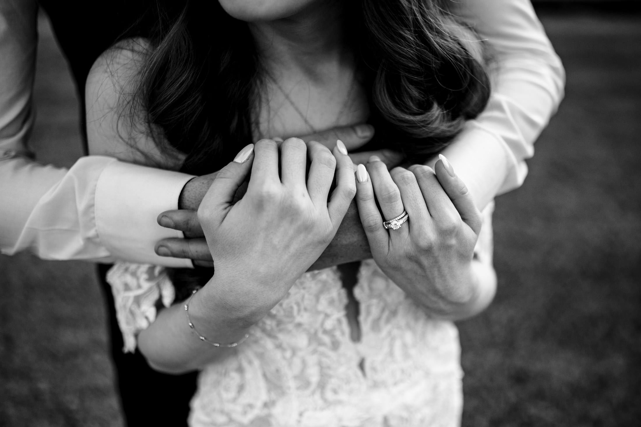 Couple embracing at Ashgrove Acres, with a lace dress and engagement ring. Black and white photo.