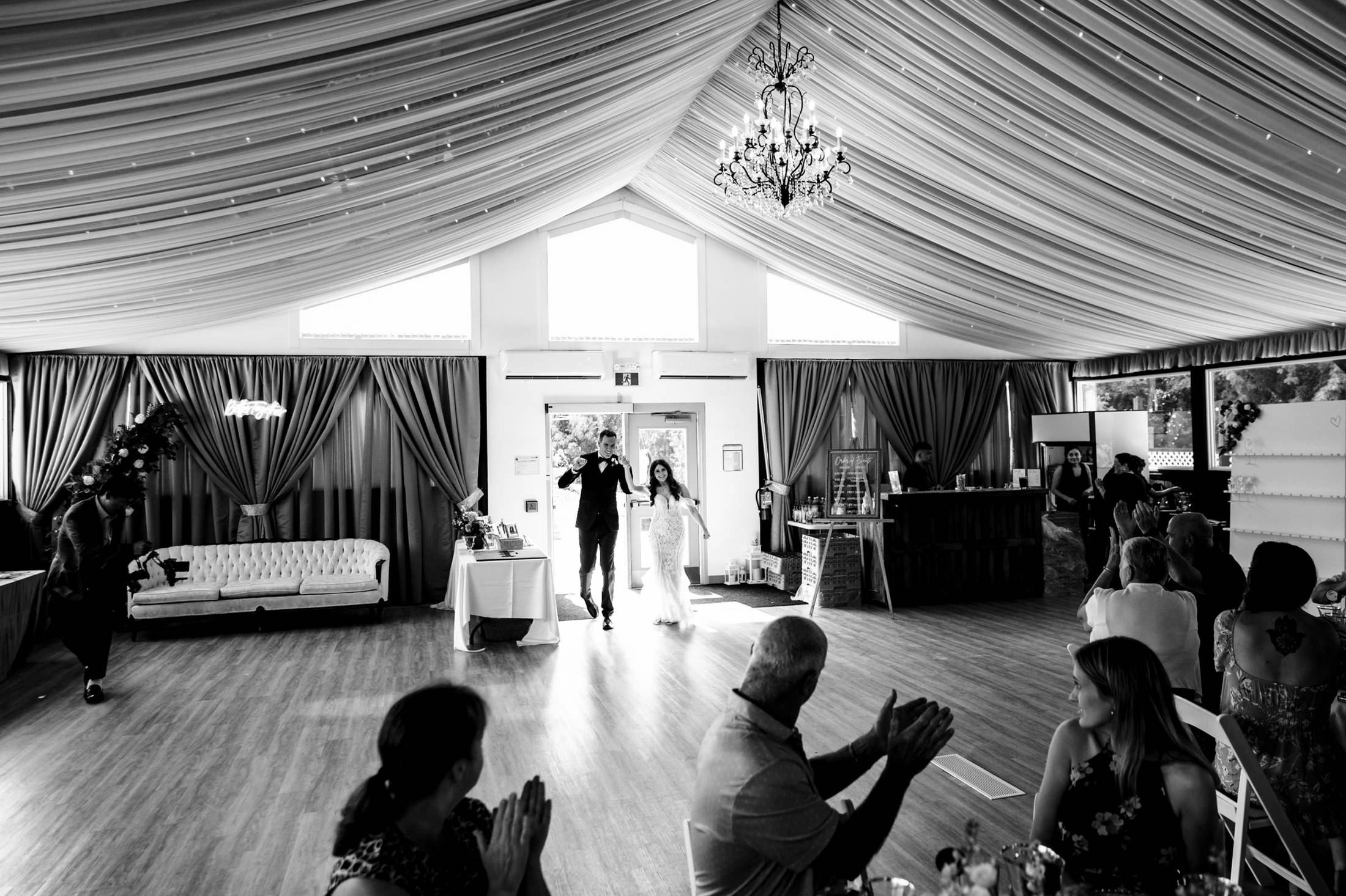 Couple enters Ashgrove Acres hall as seated guests applaud.