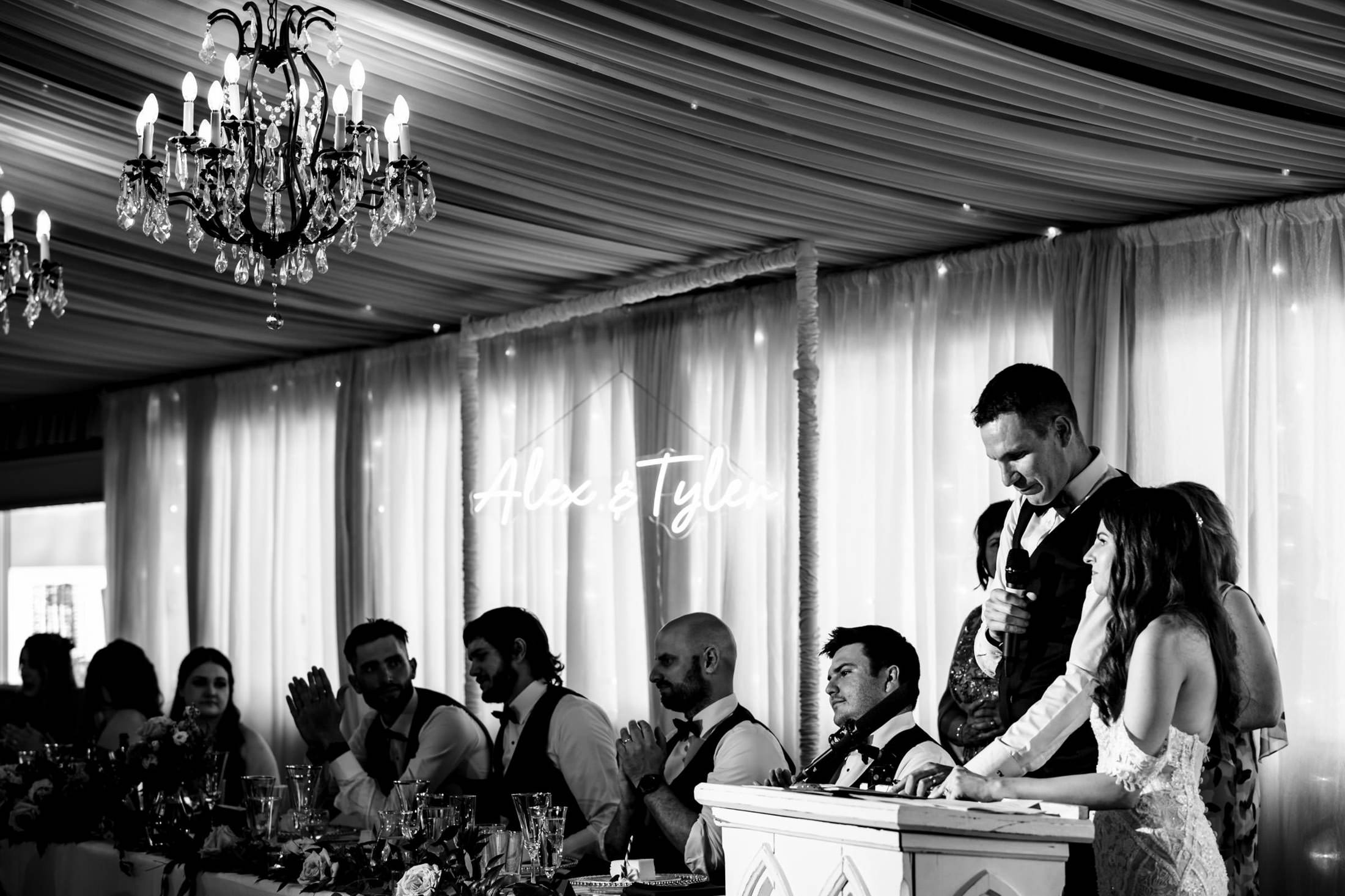 Wedding speech at Ashgrove Acres, bride and groom under chandelier at the decorated head table.