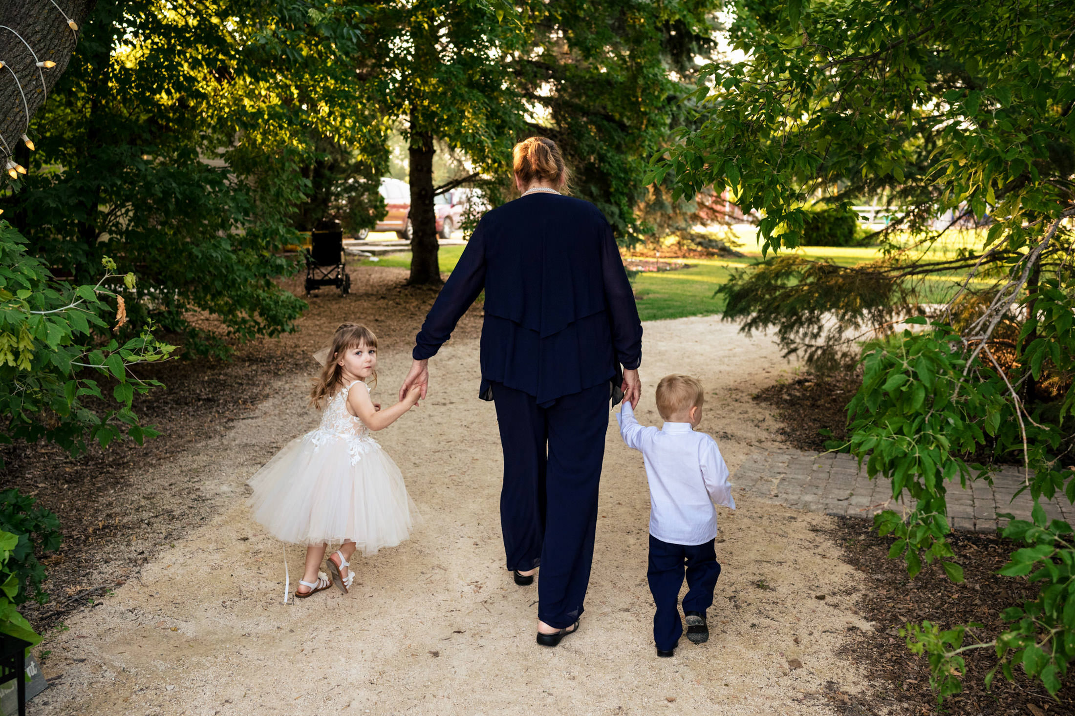 An adult and two children stroll hand in hand through Ashgrove Acres' forest path.