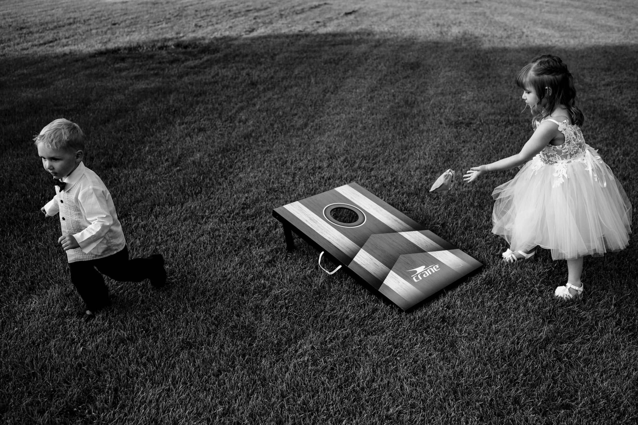 Two children at Ashgrove Acres play cornhole on grass; one tosses a bag, the other runs.
