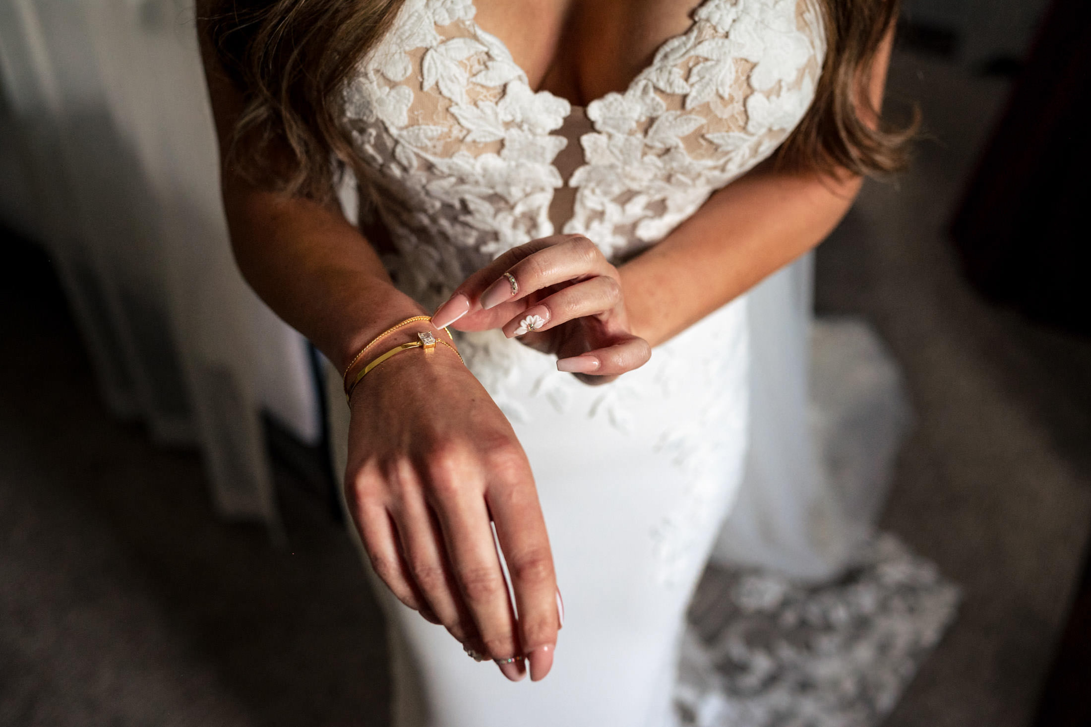 Bride adjusting bracelet on wrist, wearing white lace dress at Italian wedding in Winnipeg.
