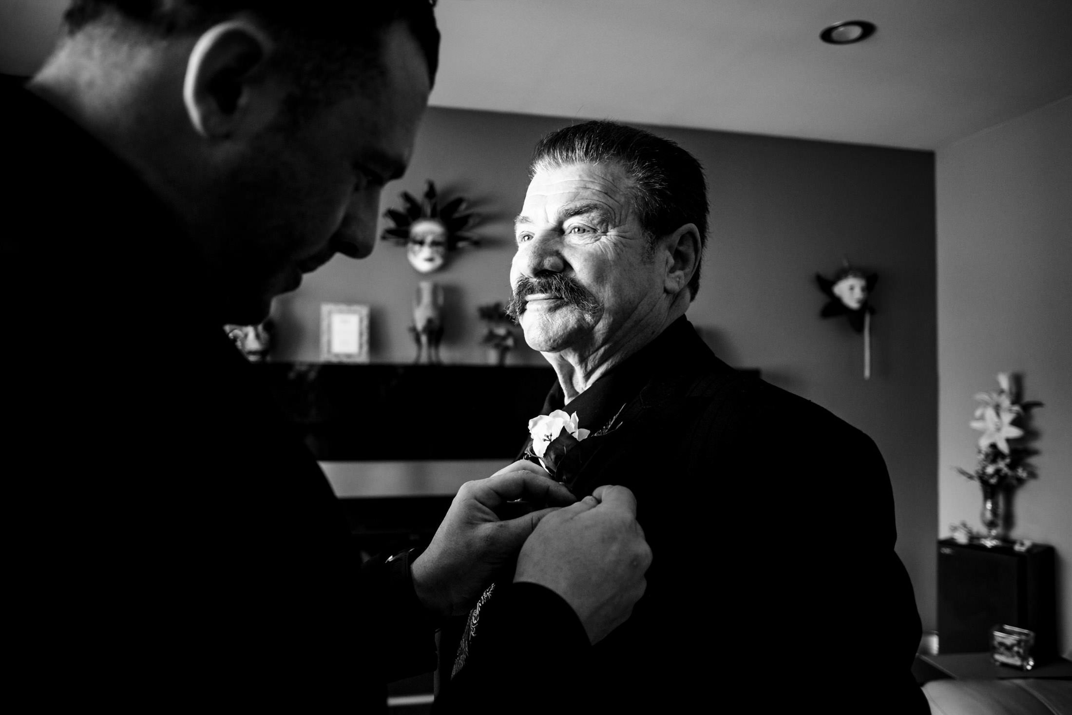 Two men in suits, one adjusting a boutonnière for an Italian wedding in Winnipeg.
