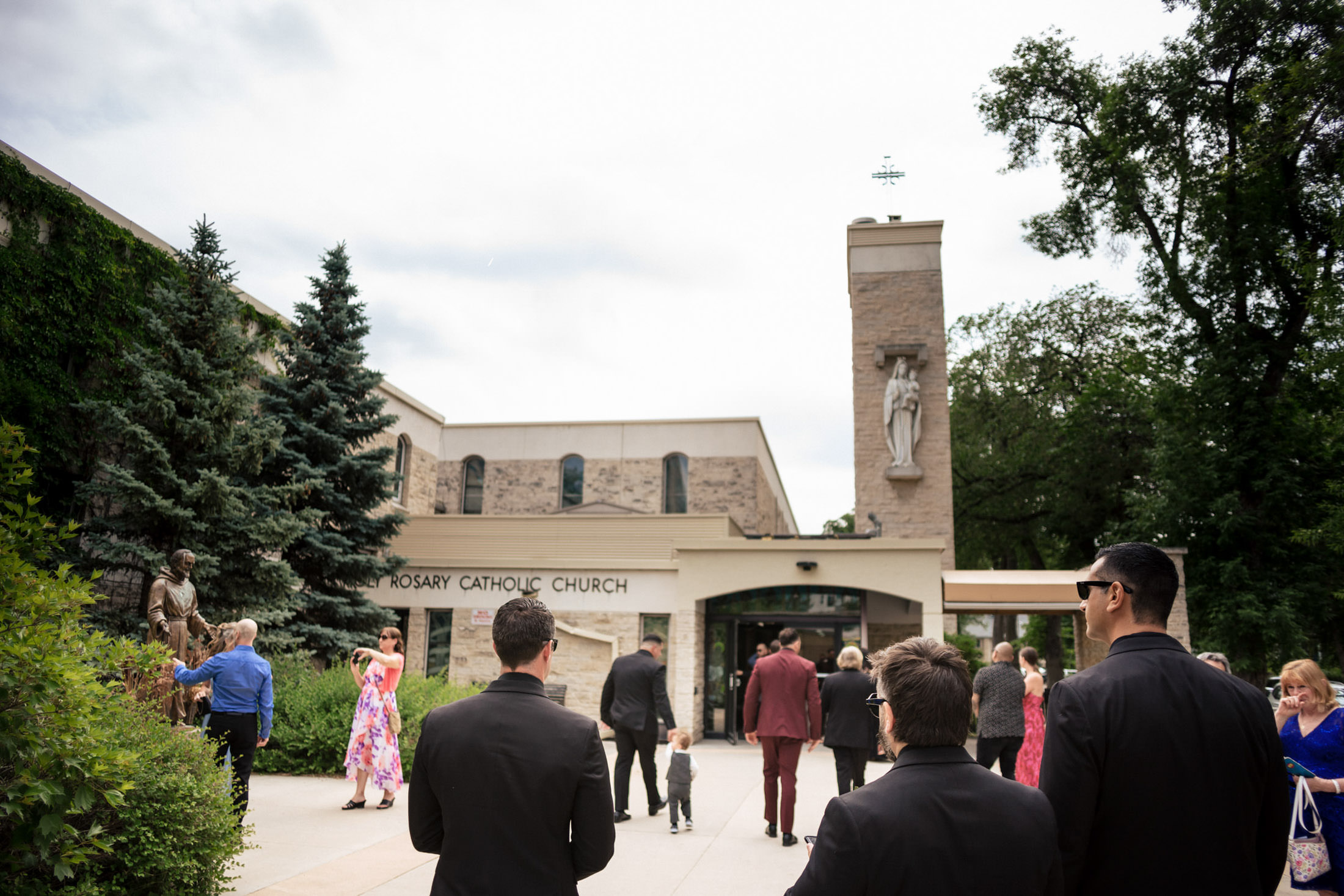 People gathered outside Rosary Catholic Church for an Italian wedding on a cloudy day.