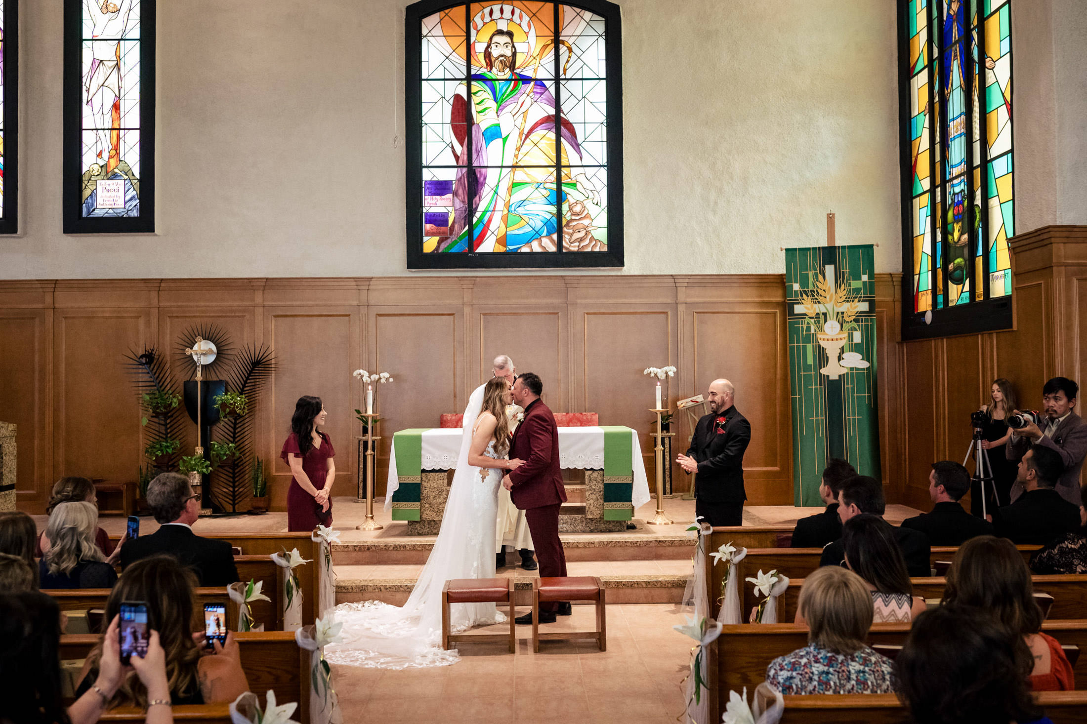Bride and groom kiss at the altar of a church in Winnipeg, with stained glass watching.
