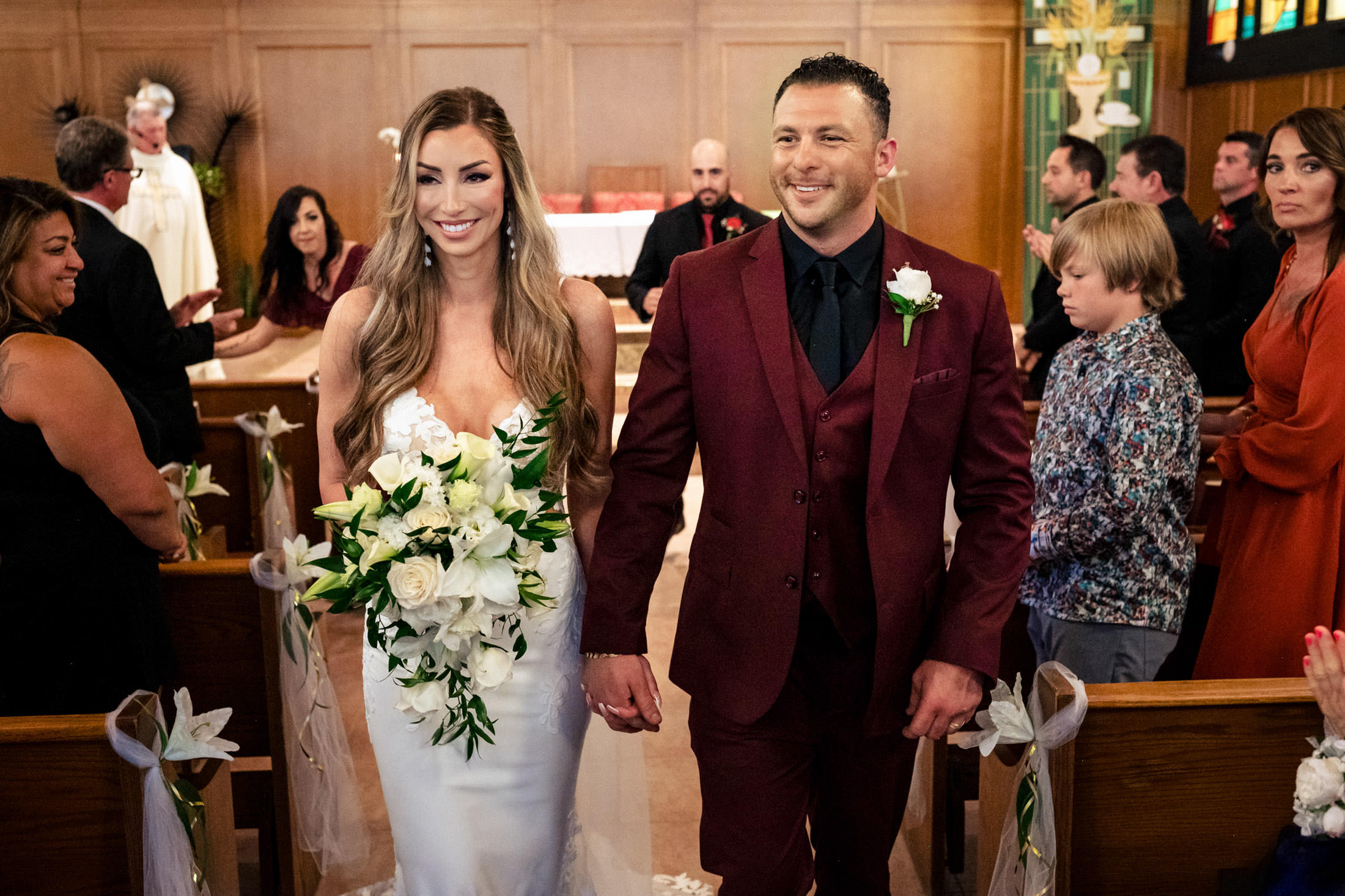 An Italian wedding in Winnipeg: A bride and groom smile, holding hands down the church aisle.