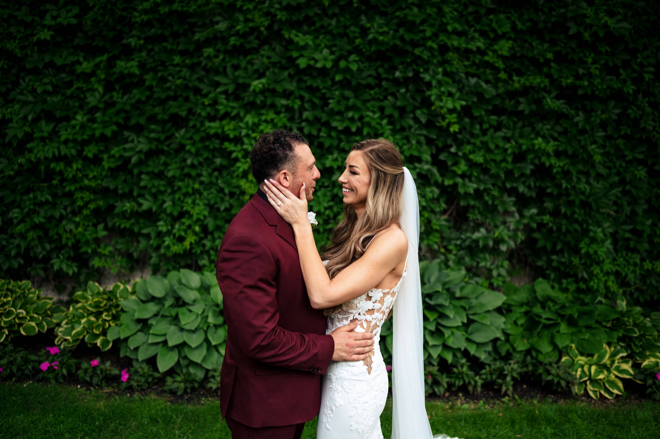 Bride and groom smiling at an Italian wedding in Winnipeg with lush green foliage.