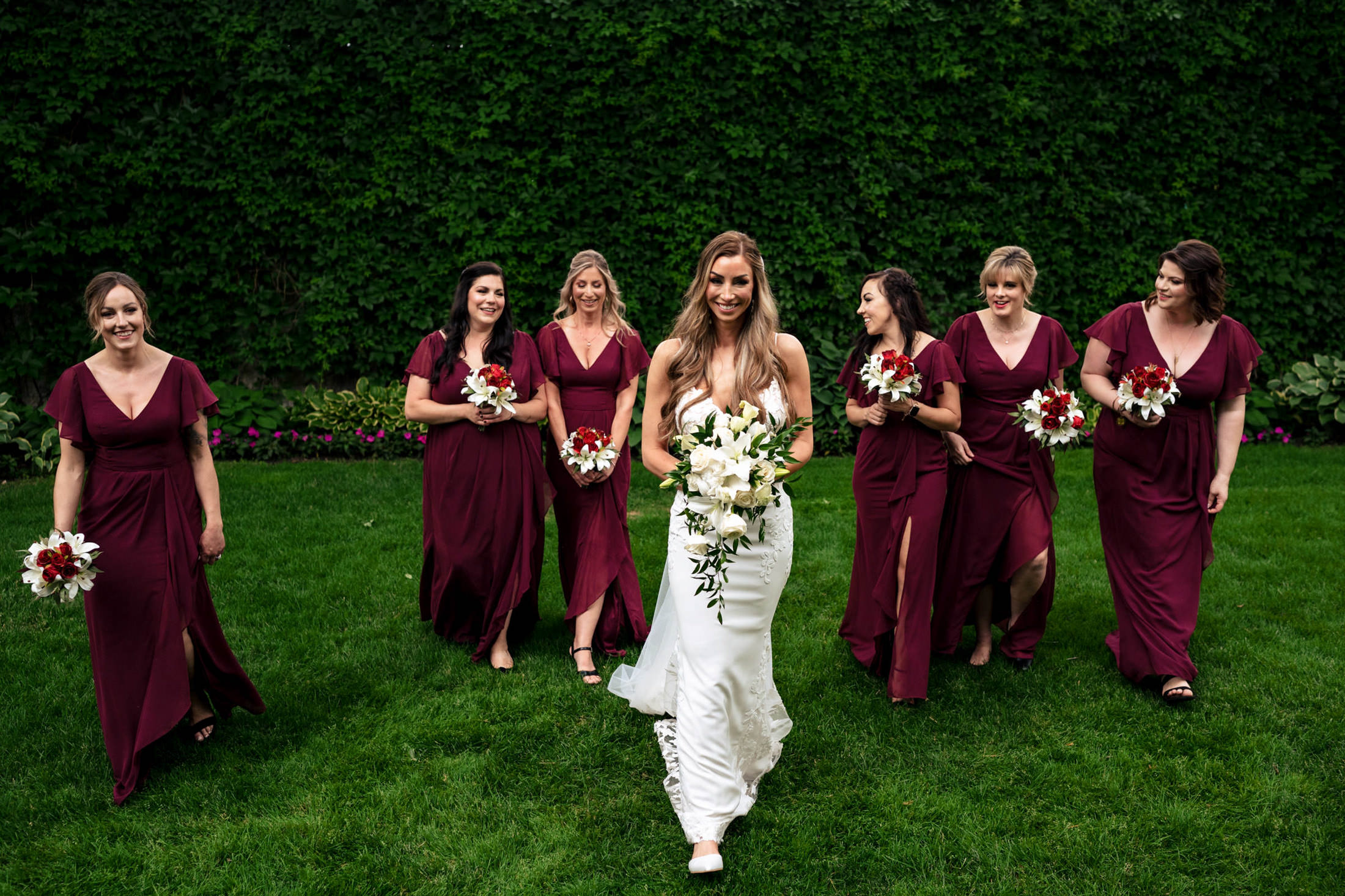 Bride in white dress walks with bridesmaids in burgundy at an Italian wedding in Winnipeg.