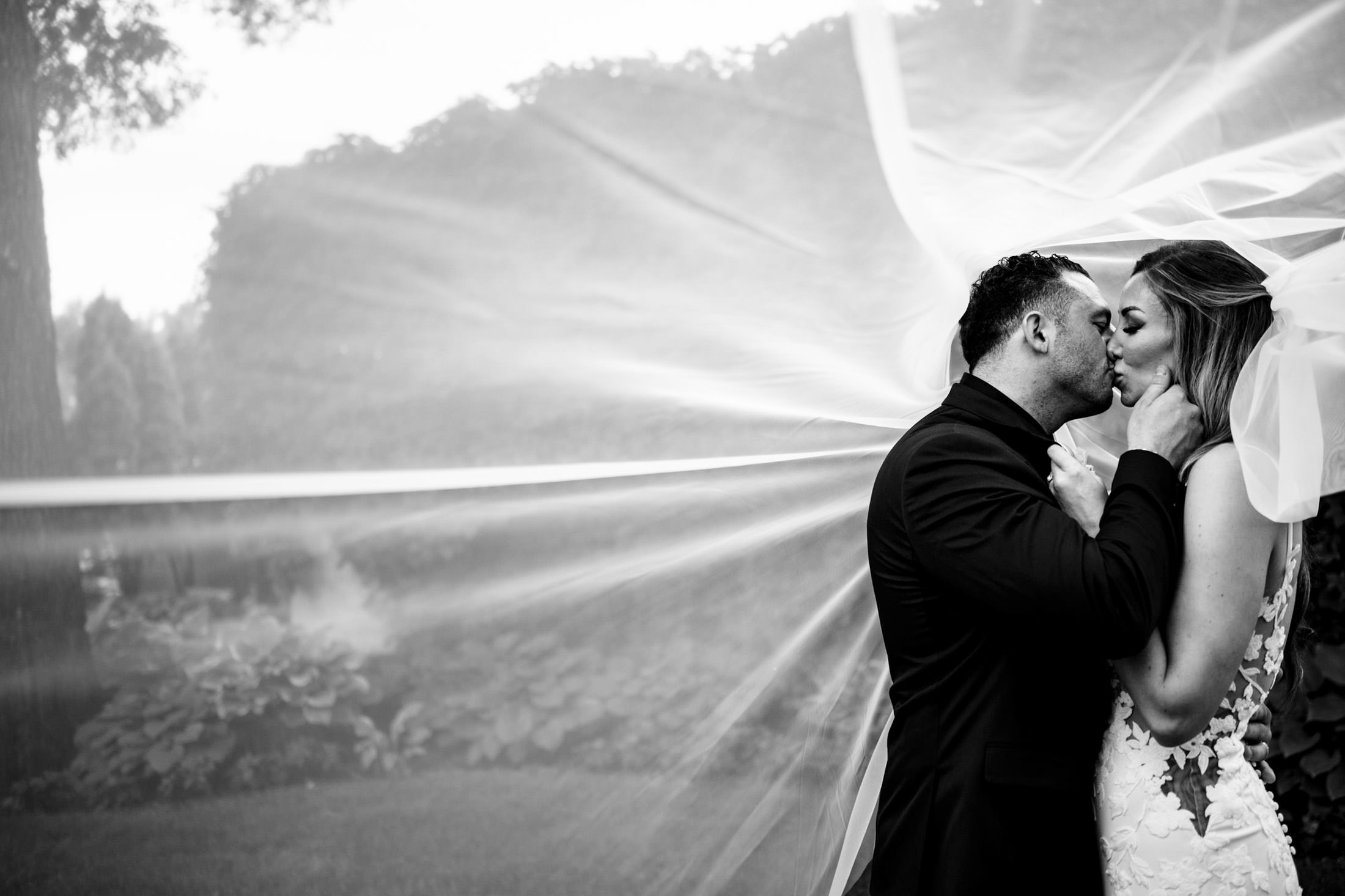 Bride and groom kissing in a garden during an Italian wedding in Winnipeg, veil flowing behind.