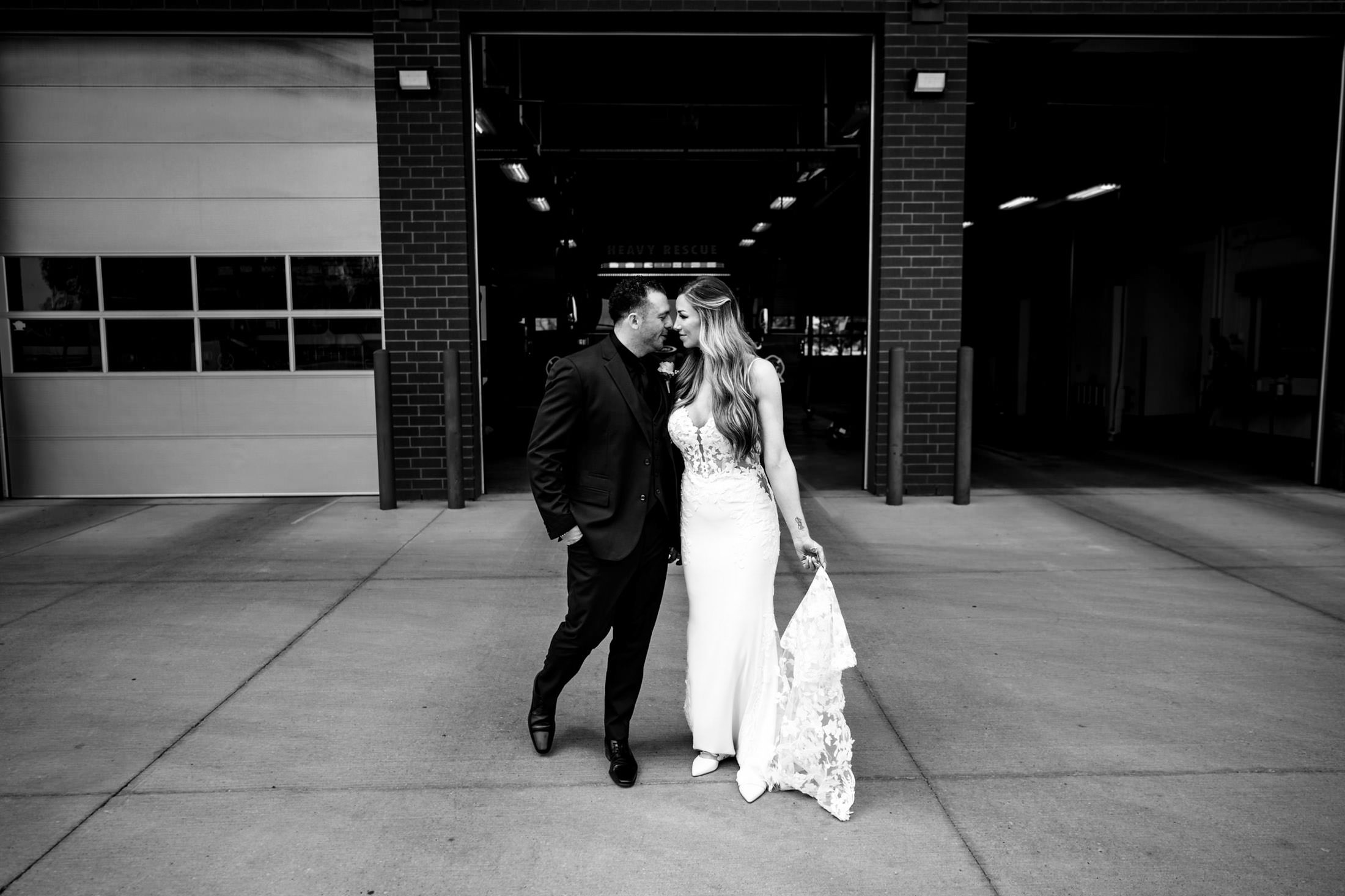 Bride and groom at an Italian wedding, smiling by an industrial building entrance.