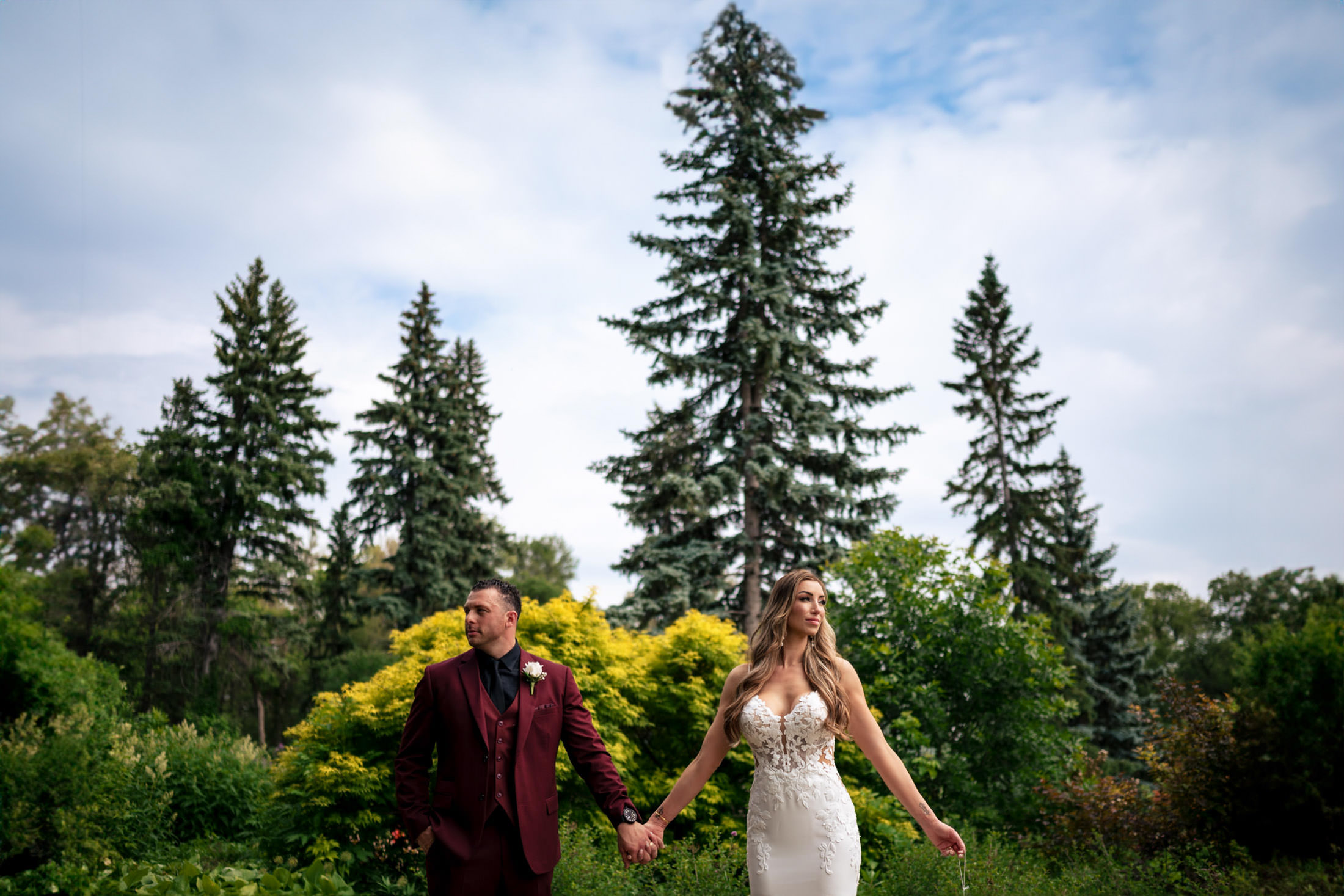 Couple at an Italian wedding in a garden, surrounded by tall trees, wearing formal attire.