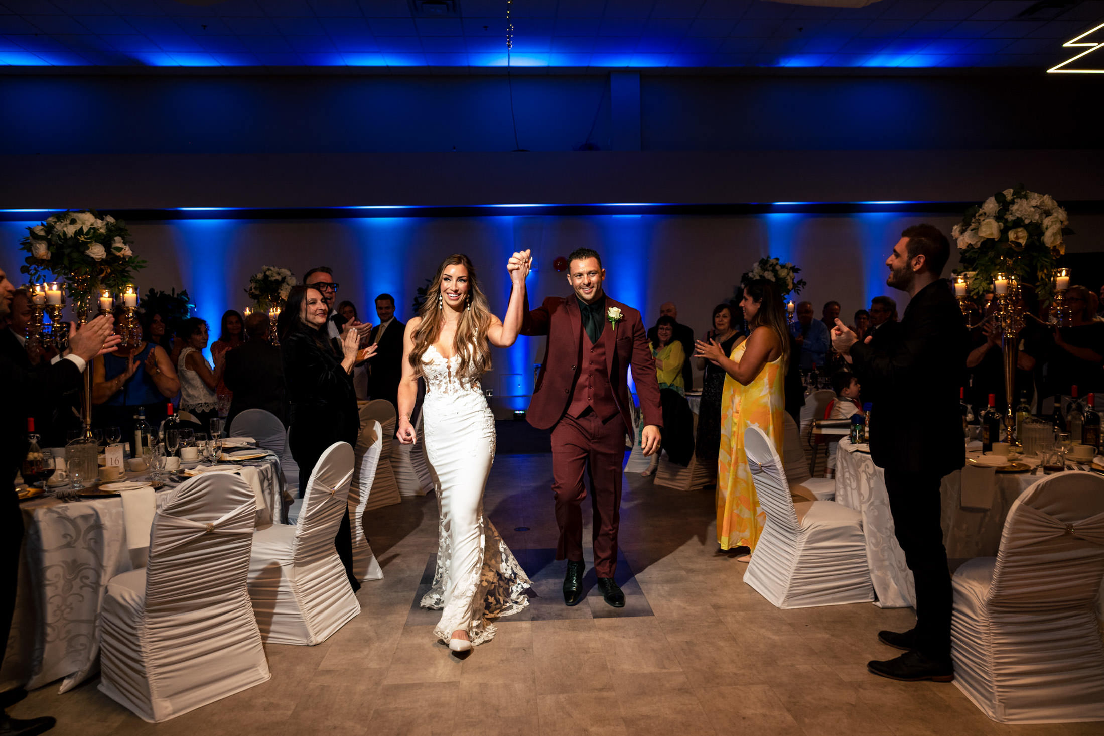 The bride and groom hold hands, entering their Italian wedding in Winnipeg as guests applaud.