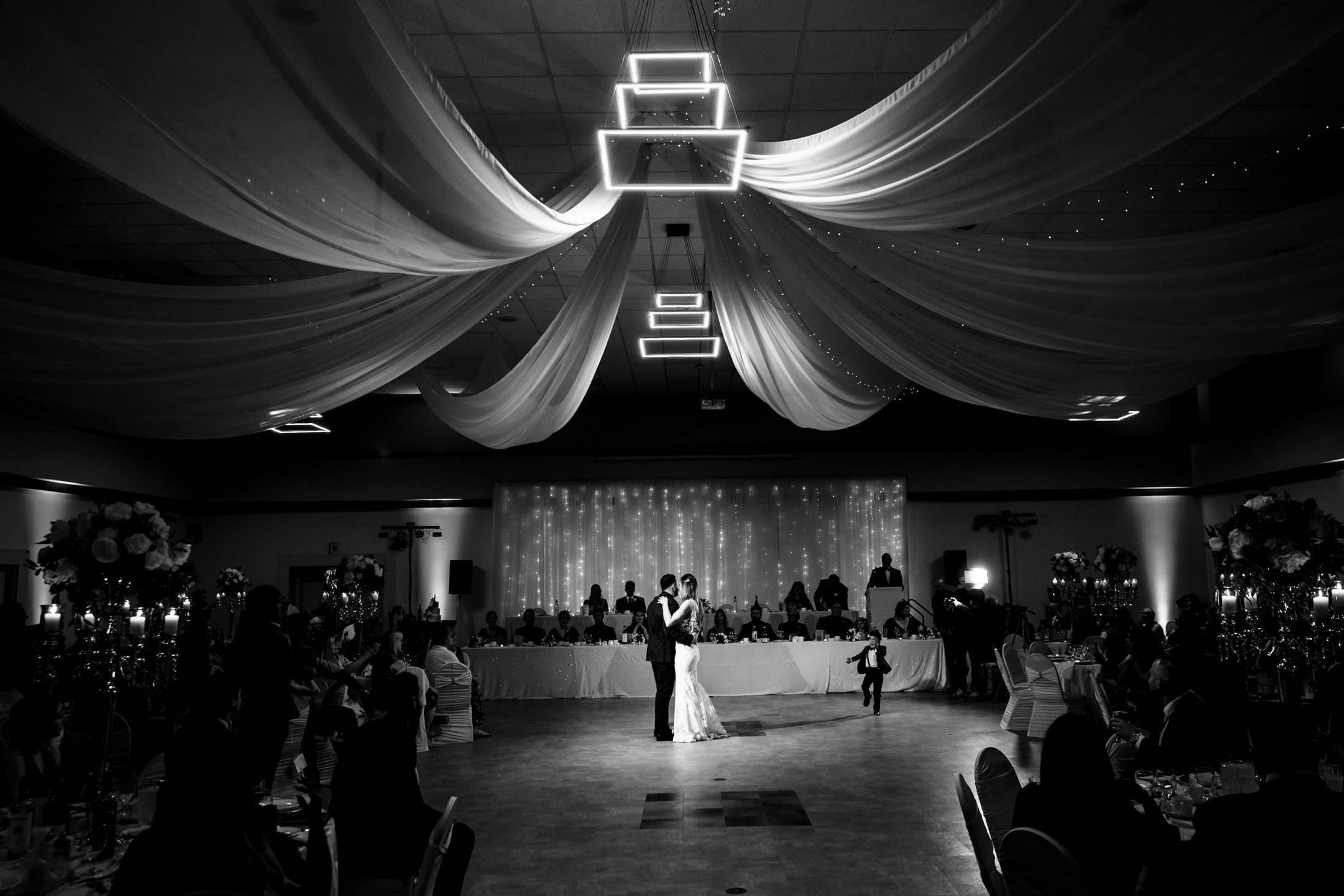 An Italian wedding couple dances under draped fabric and lights in an elegant ballroom.