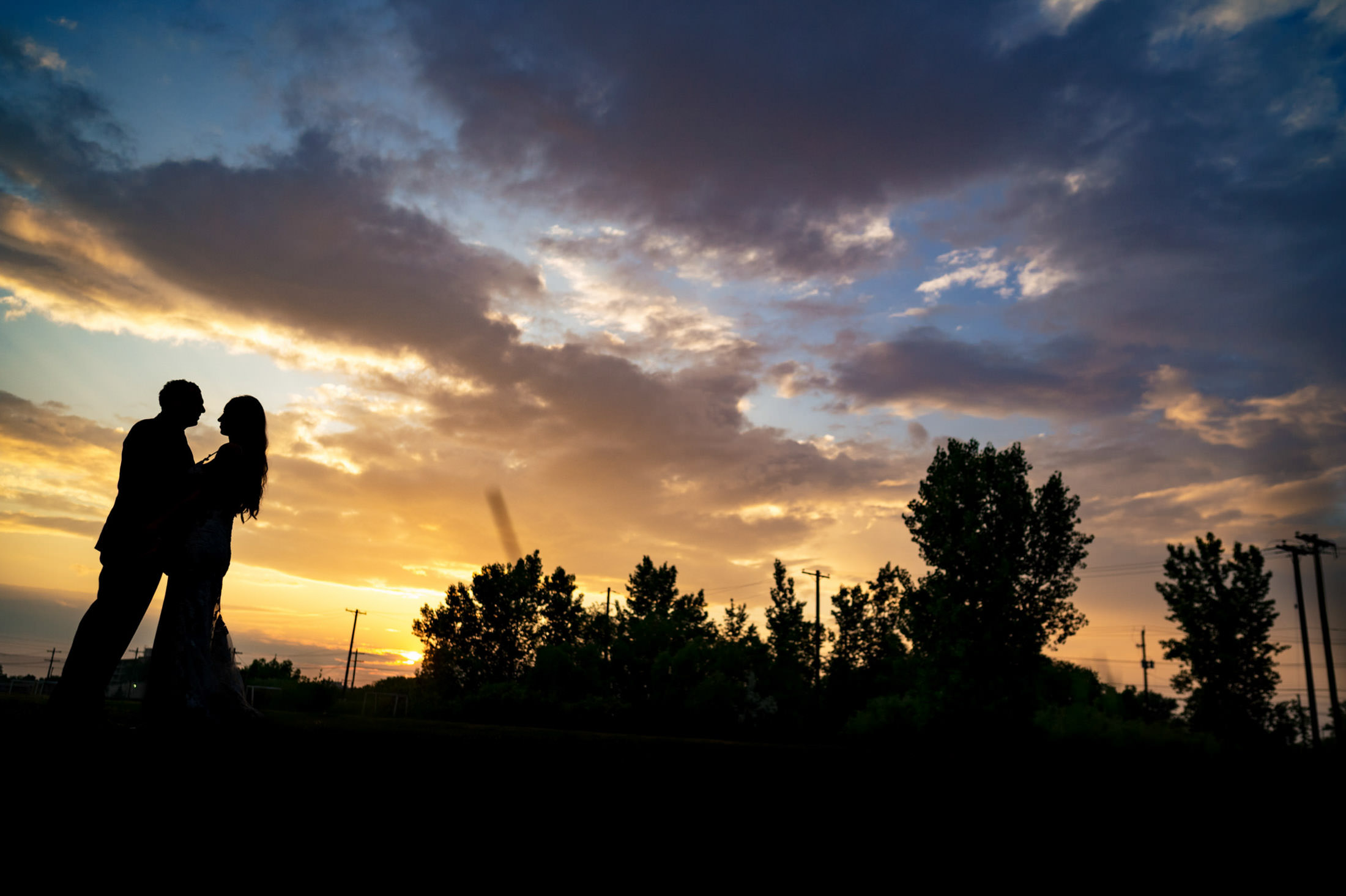 Silhouetted couple embraces under Winnipeg's vibrant sunset at their Italian wedding.
