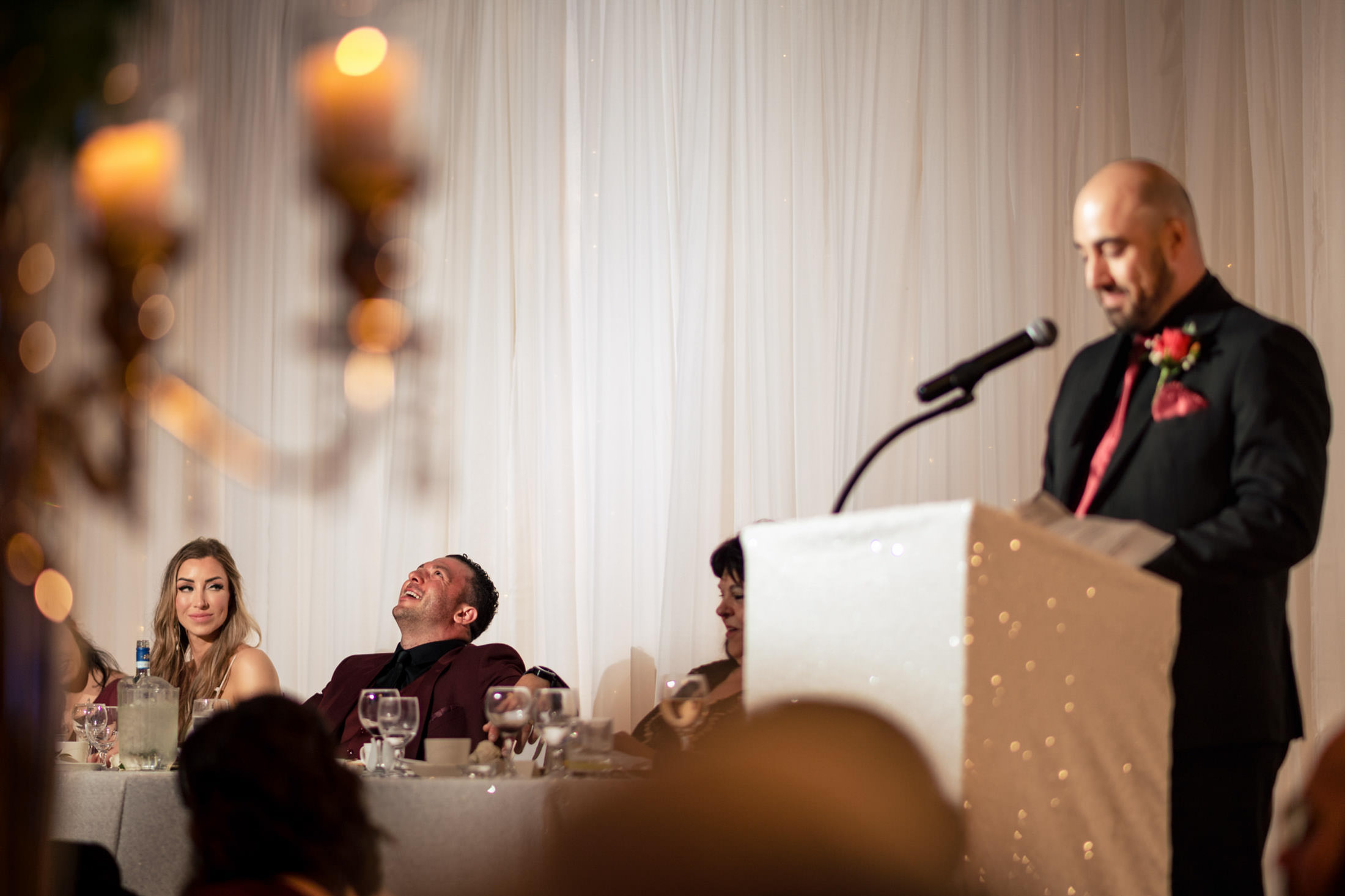 Man speaking at podium; guests smiling and laughing at an Italian wedding in Winnipeg.