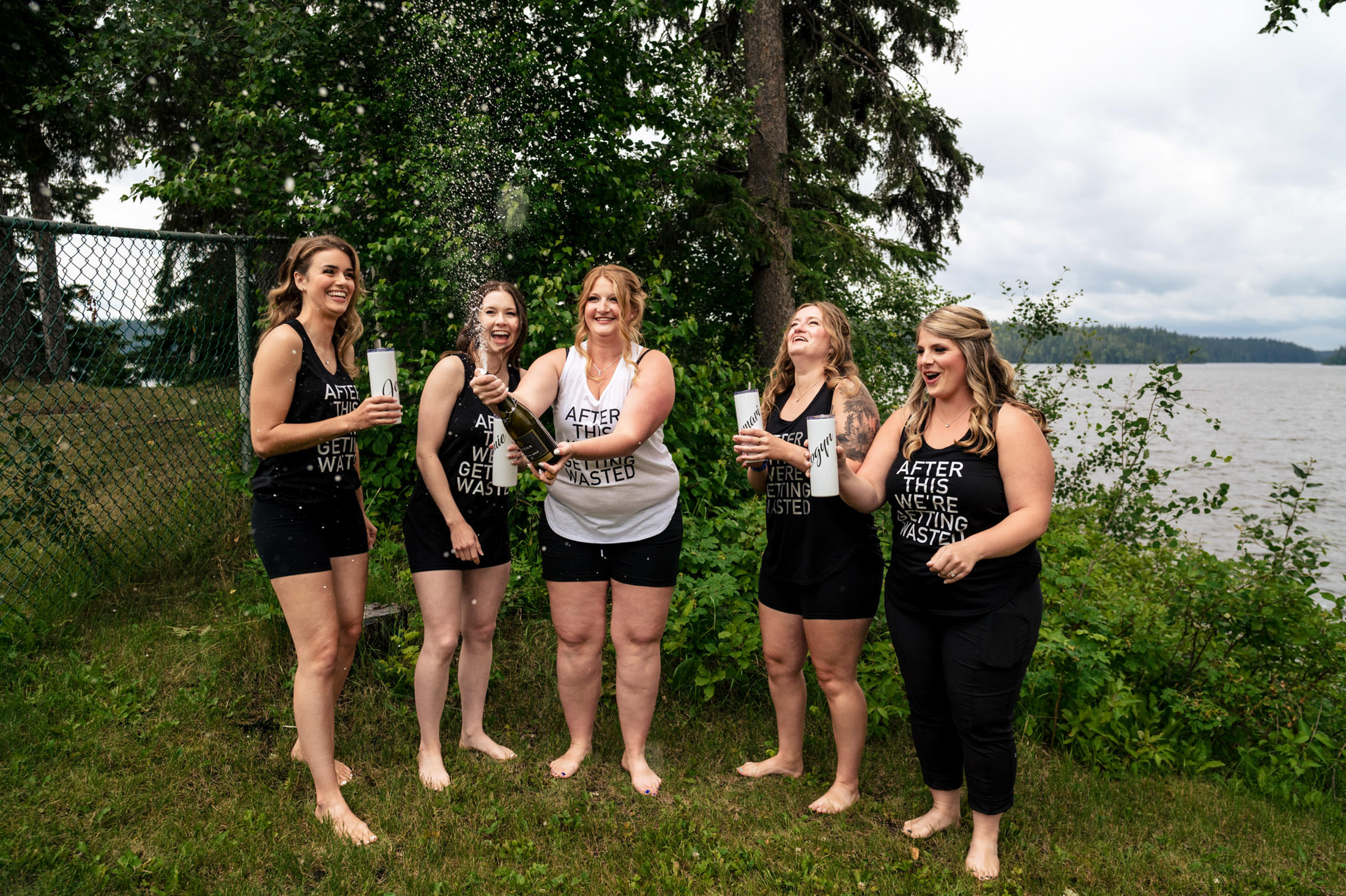 Five women in matching outfits celebrate with champagne by Snow Lake.
